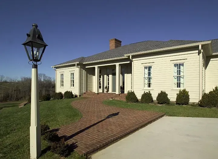 Cream-colored house with a brick walkway, a lamppost, and a bright blue sky.