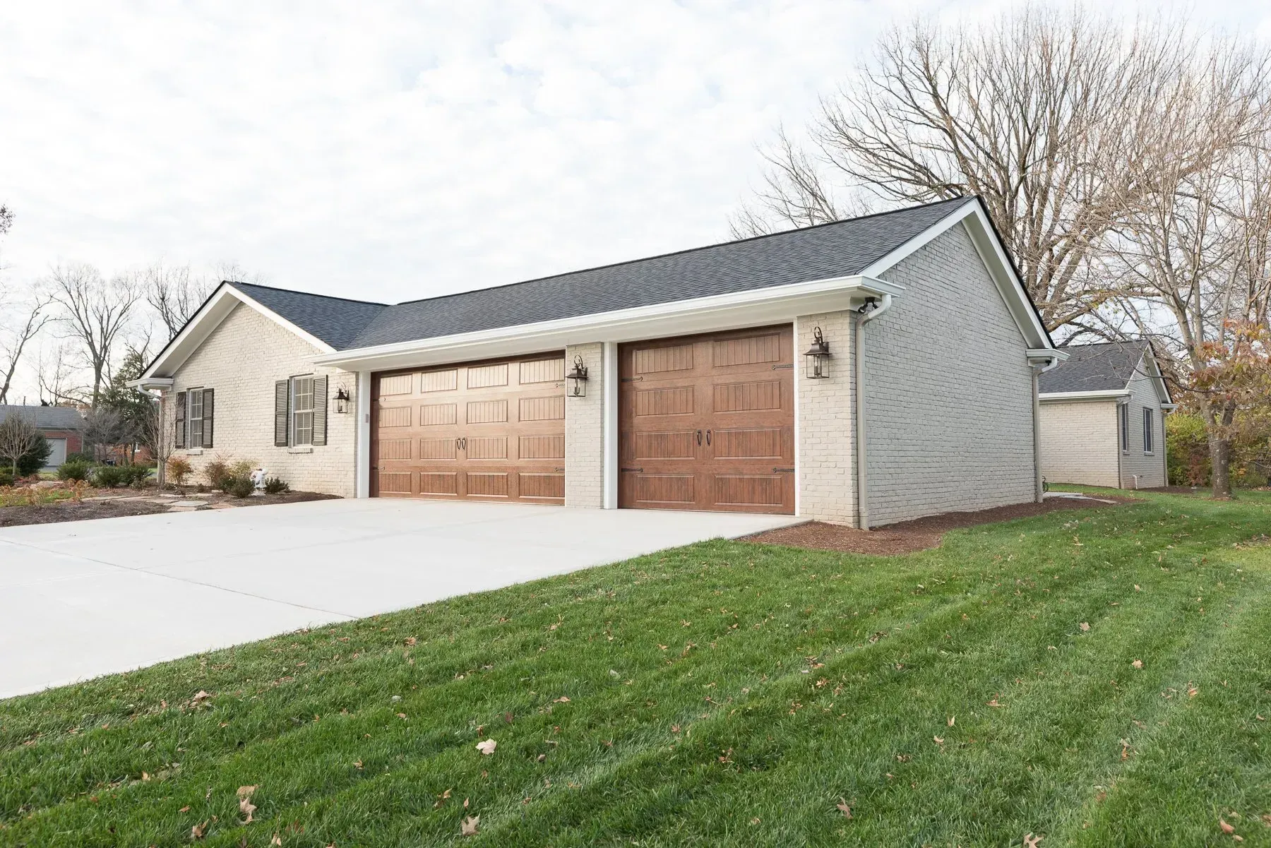 Tan house with a two-car garage, brown garage doors, and concrete driveway on a grassy hill.