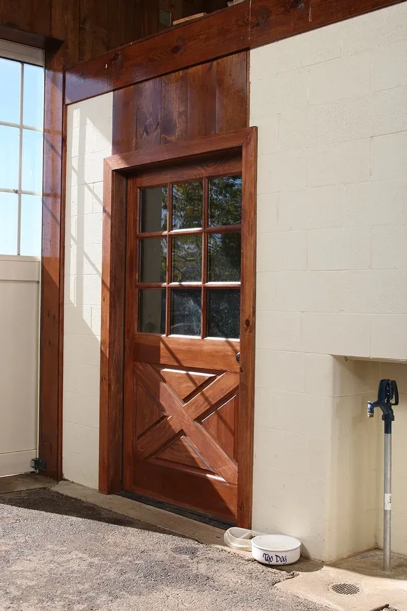 Wooden door with glass panes and decorative cross design, set in a light-colored wall.