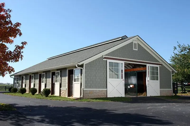 Horse stable, gray siding, white doors, asphalt drive, clear sky.