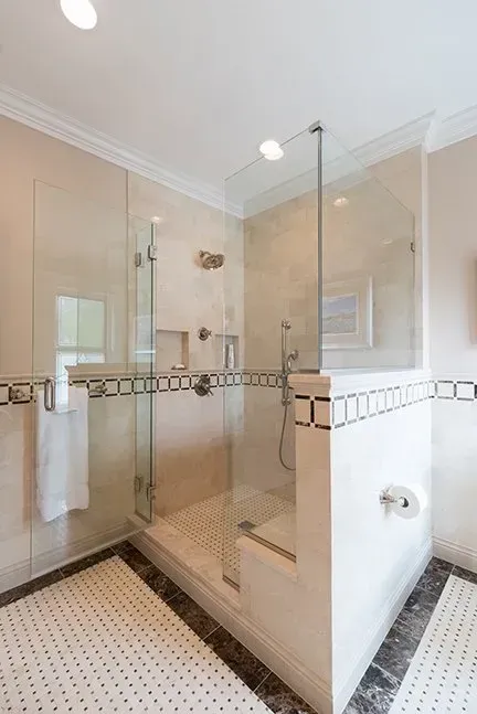 Bathroom with corner glass shower. Beige tile walls, white and black tile floor. Towel and toilet paper visible.