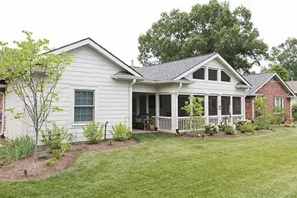White house with a screened porch and red brick section, surrounded by green lawn and trees.