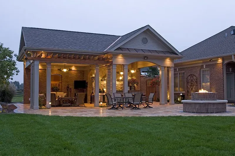 Outdoor patio with seating, fireplace, and brick home at dusk.
