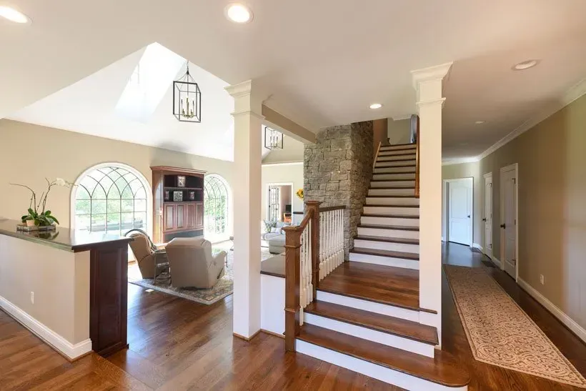 Entryway with stairs, stone wall, and seating area with arched windows. Wooden floors and neutral walls.