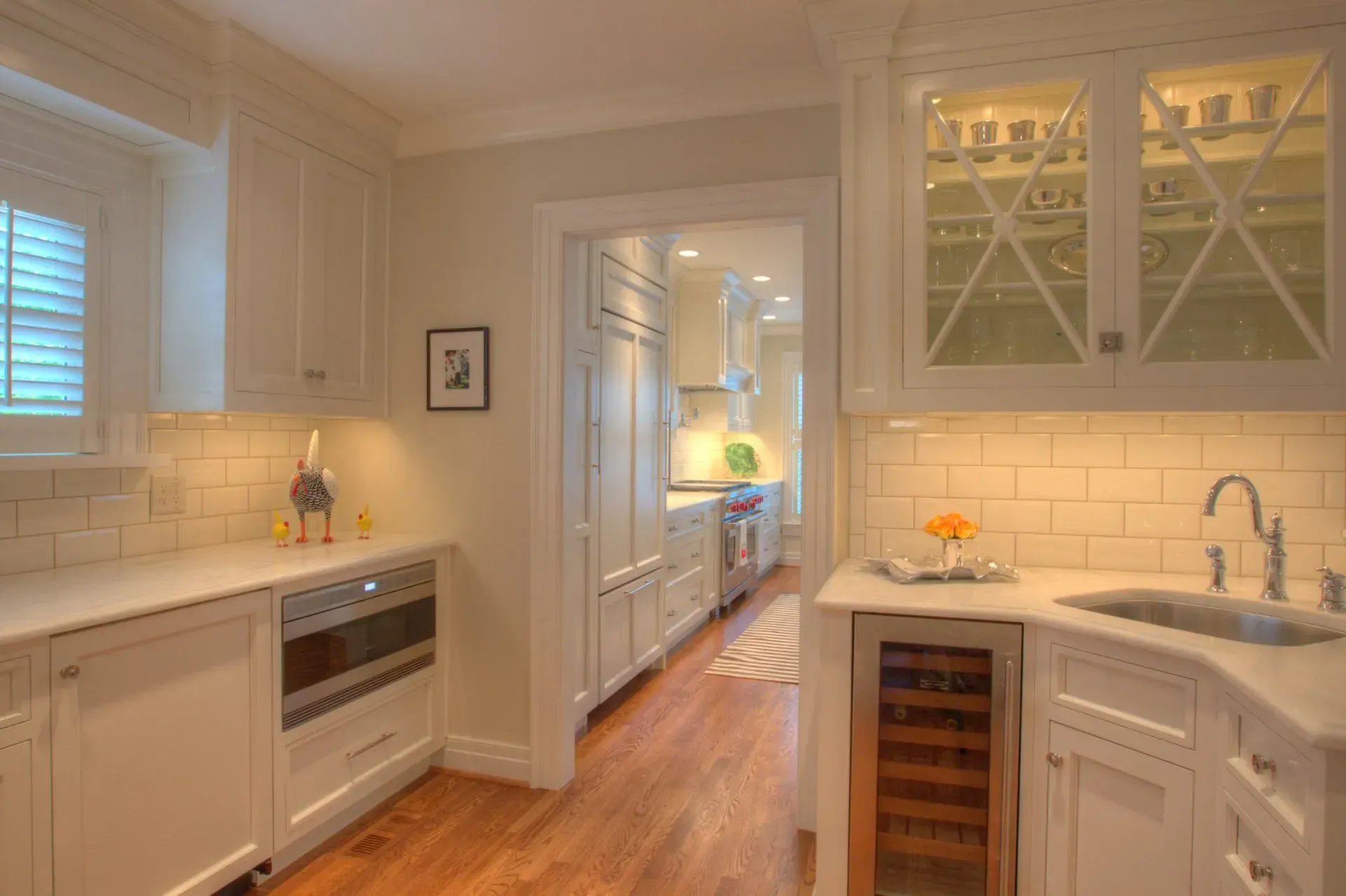 White kitchen with wood floors, built-in appliances, and a hallway leading to another part of the kitchen.