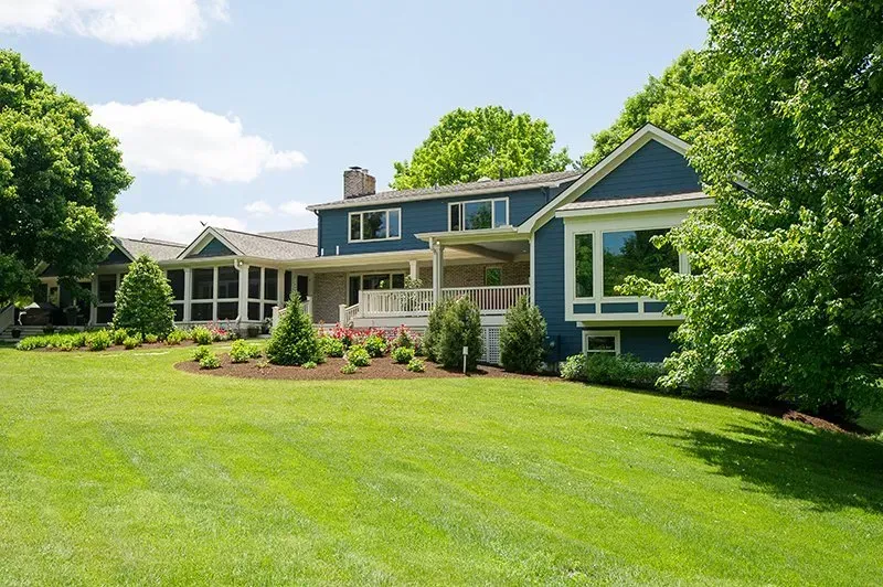 Blue house with large green lawn, surrounded by trees.