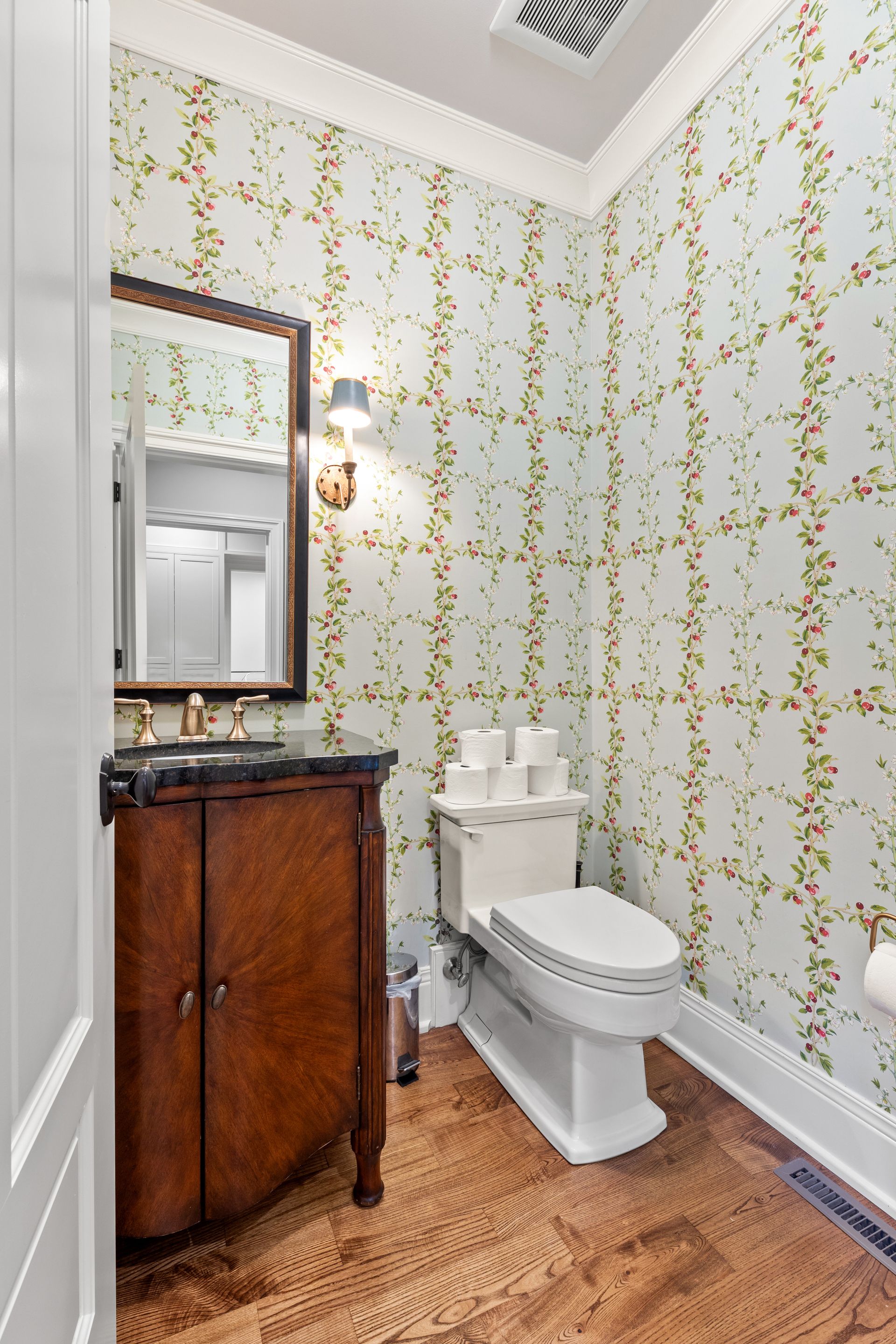Powder room with floral wallpaper, dark wood vanity, and white toilet on a brown floor.