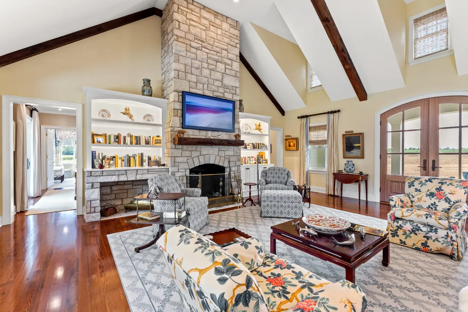 Living room with stone fireplace, TV, bookshelves, floral furniture, wood floors, and arched doorway.
