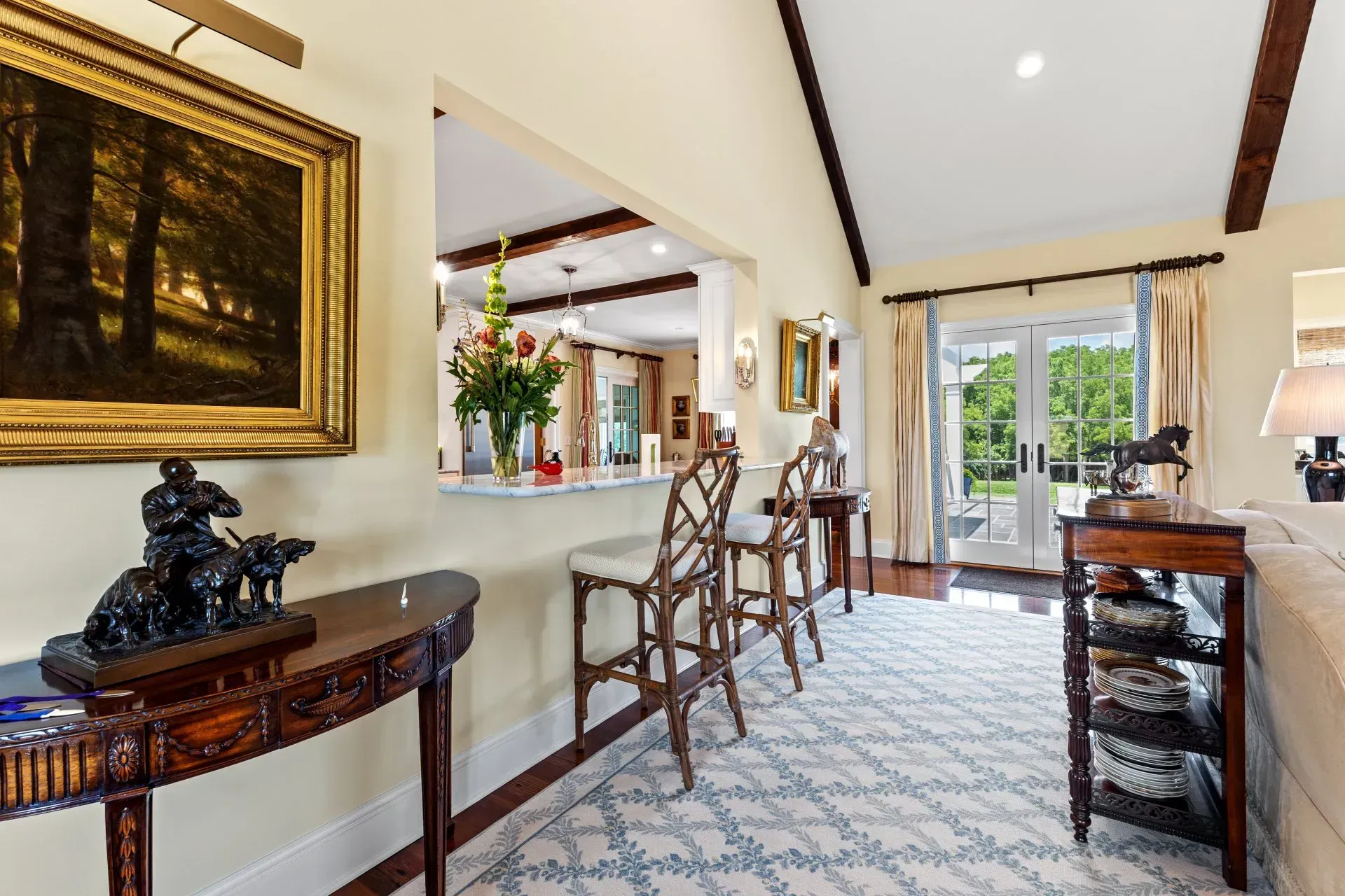 Living room with bar seating, art, and doorway to a yard, with cream walls, and a blue and cream rug.