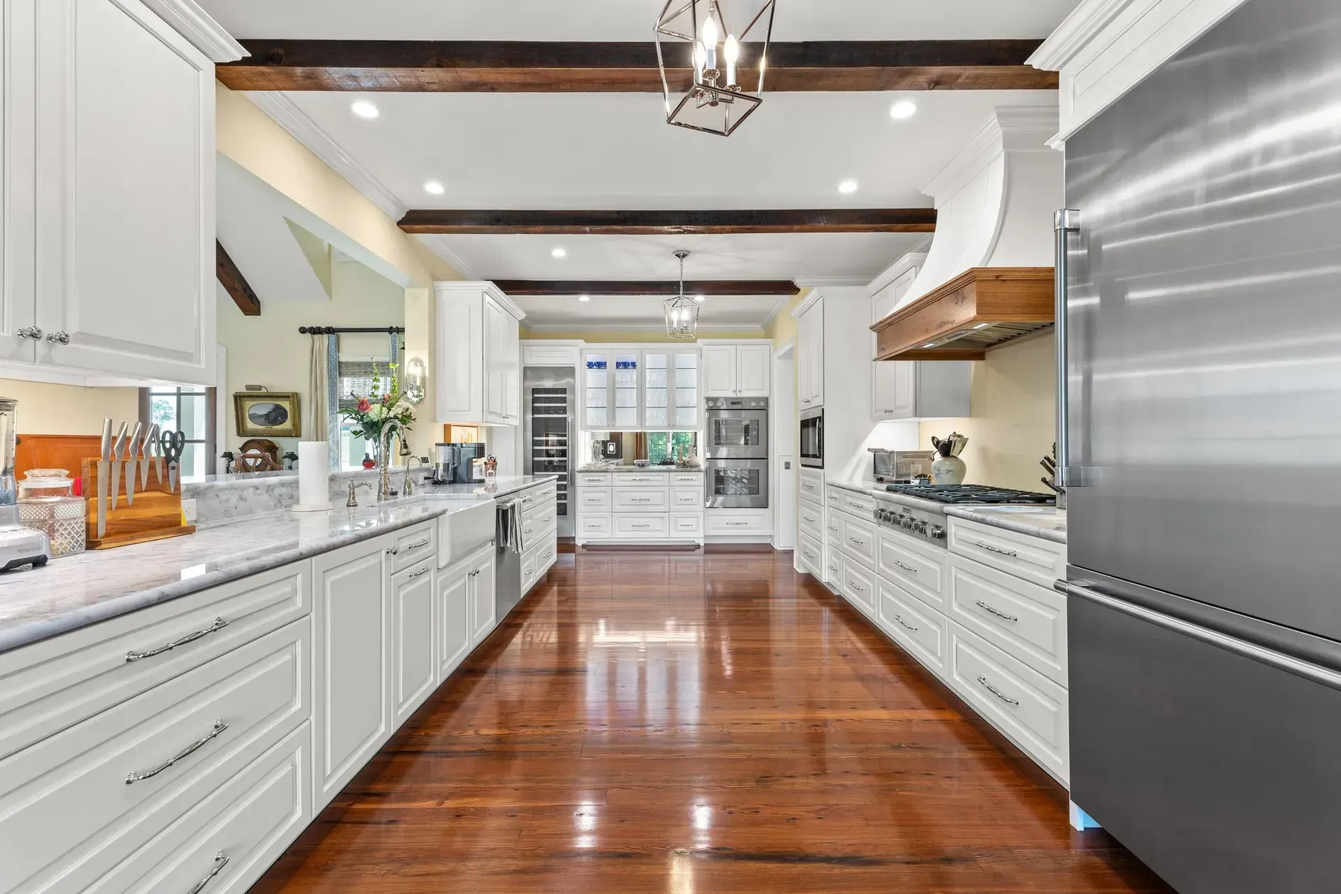 Spacious white kitchen with wood floors, stainless steel appliances, and wooden beams.