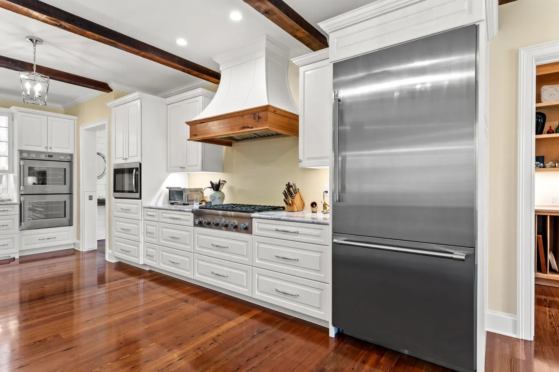 White kitchen with stainless steel refrigerator, wooden beams, and hardwood floor.