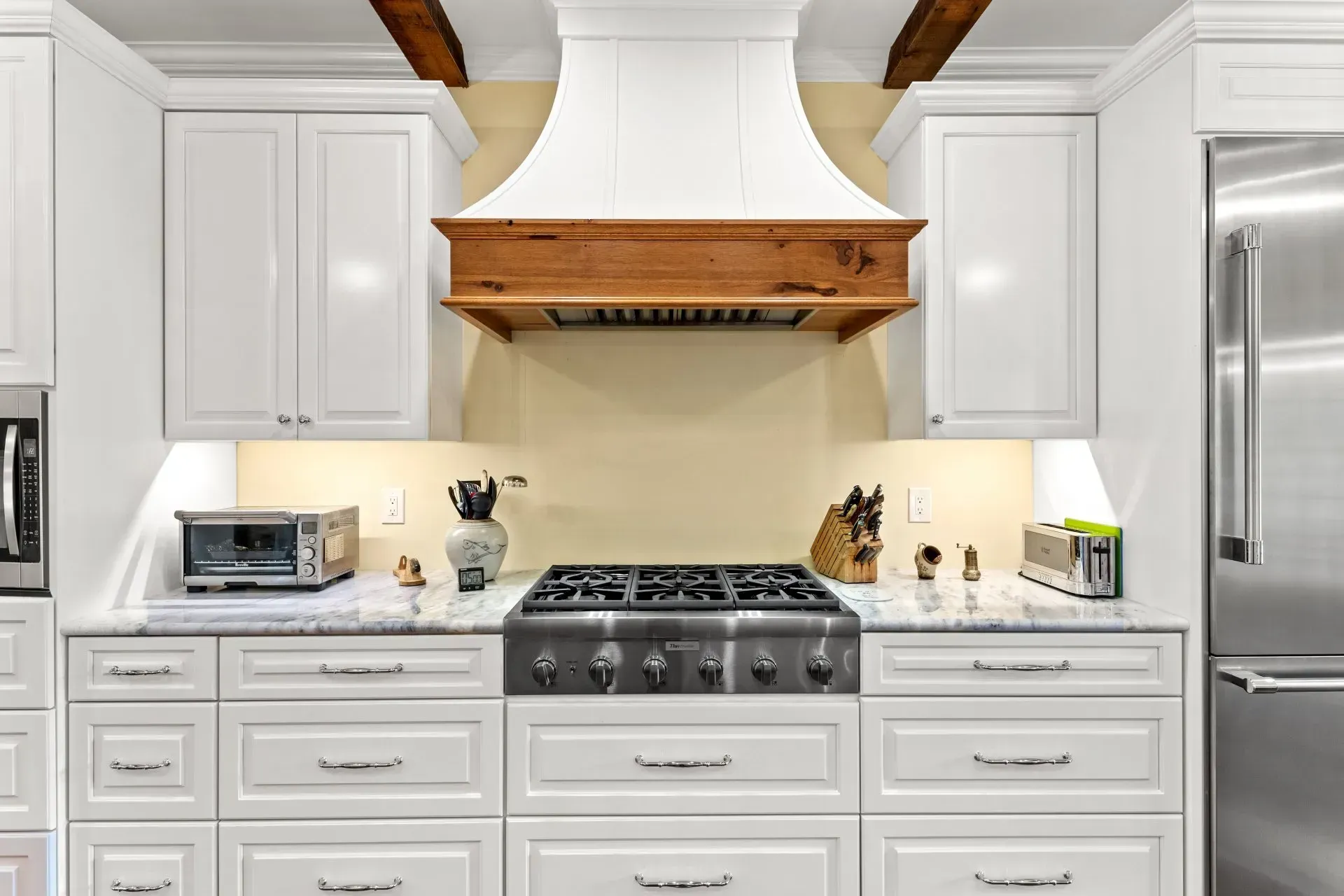 White kitchen with a stainless steel stove, hood, and appliances; wood beams and accents.