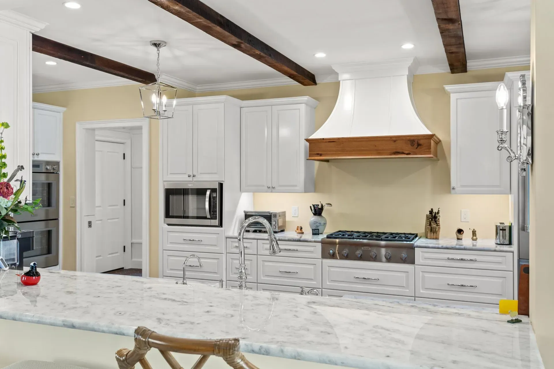 White kitchen with marble countertop, stainless steel appliances, and wooden beams.