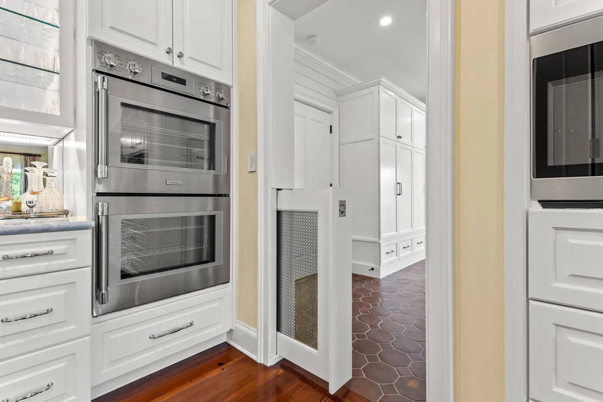 Kitchen with double ovens, a doorway with a small pet gate, and white cabinets.