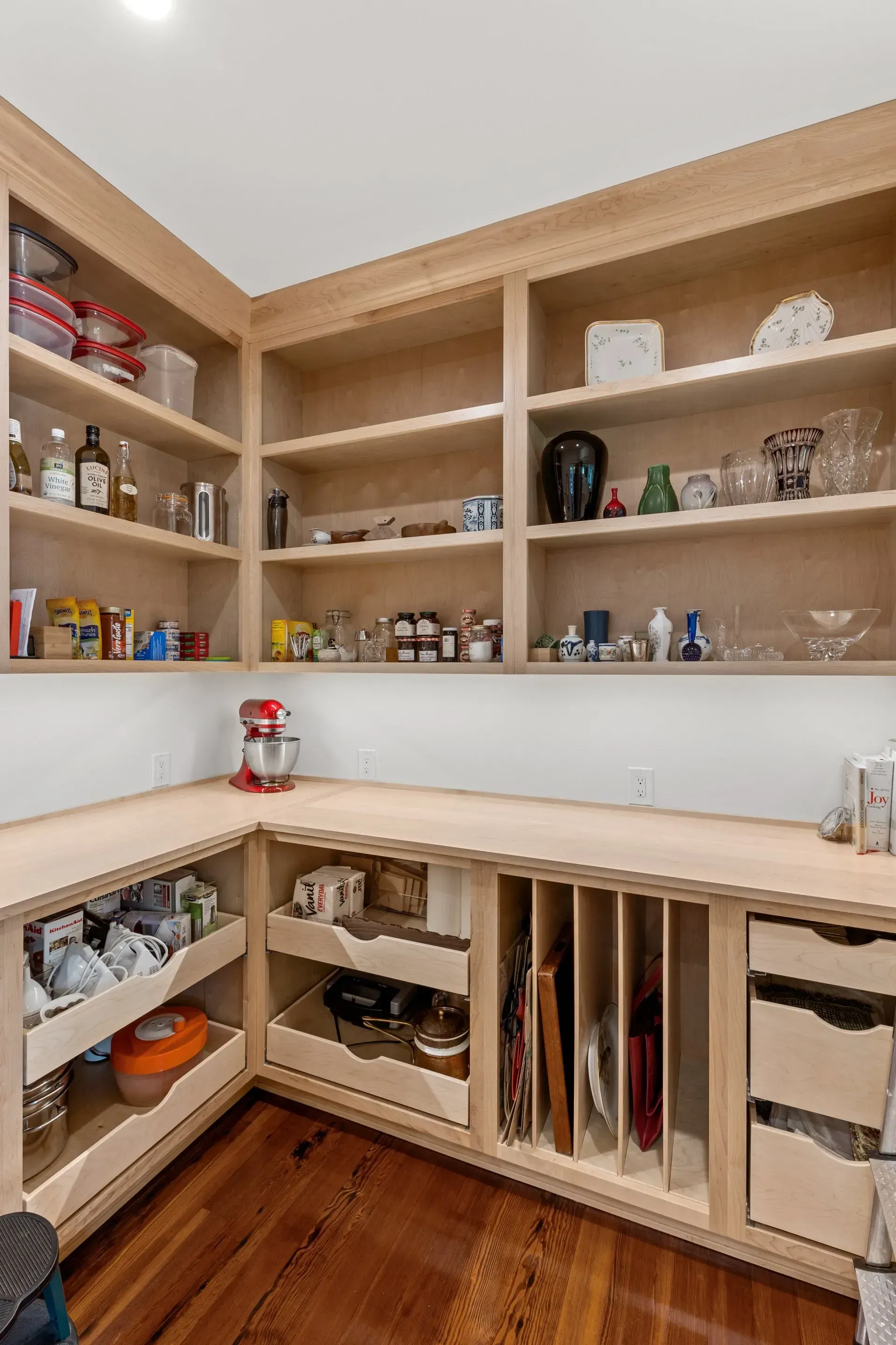 Pantry with light wood shelves and cabinets, filled with food, kitchenware, and a red stand mixer.