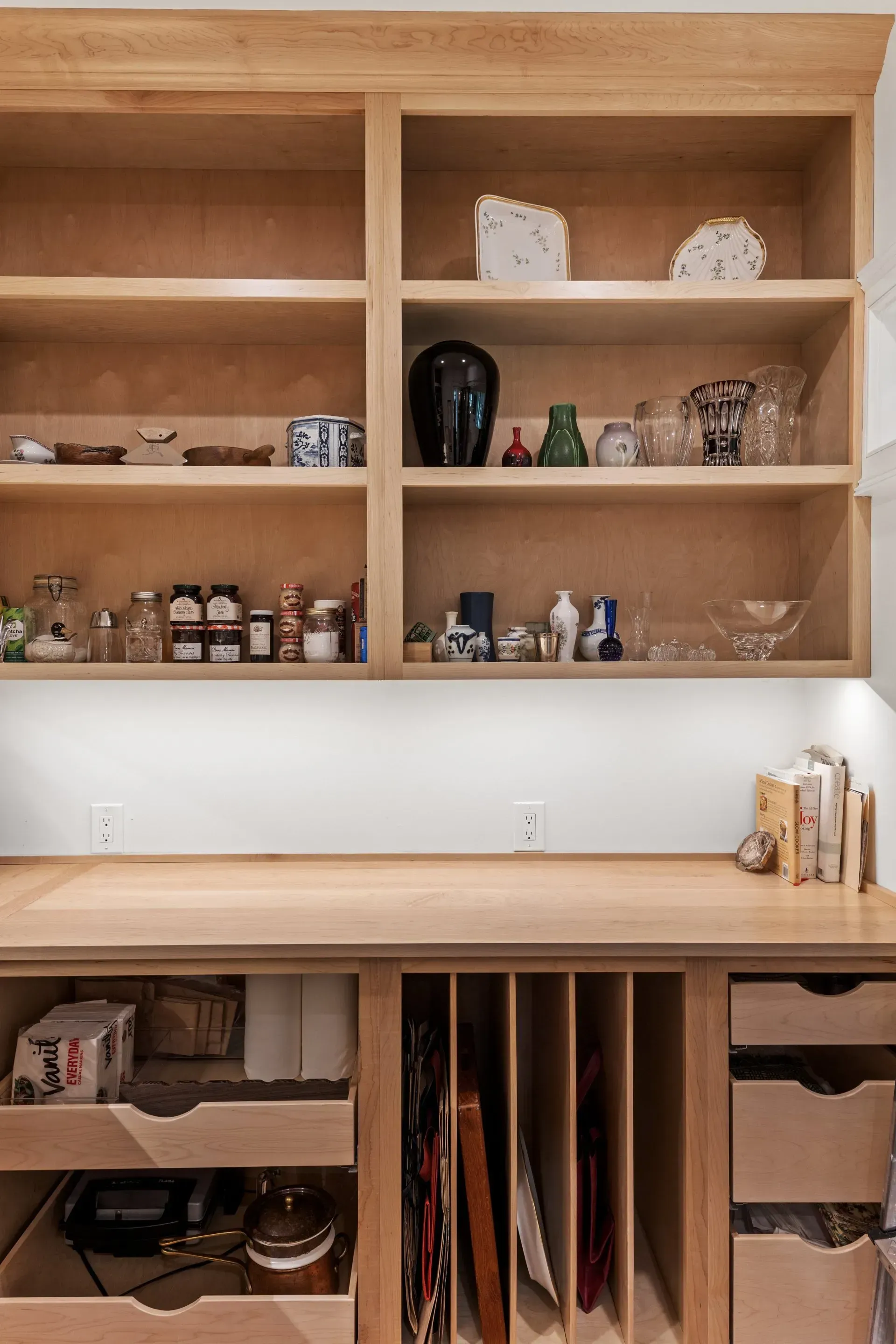 Built-in wooden shelves with various objects, including vases and jars, above a desk with drawers and dividers.