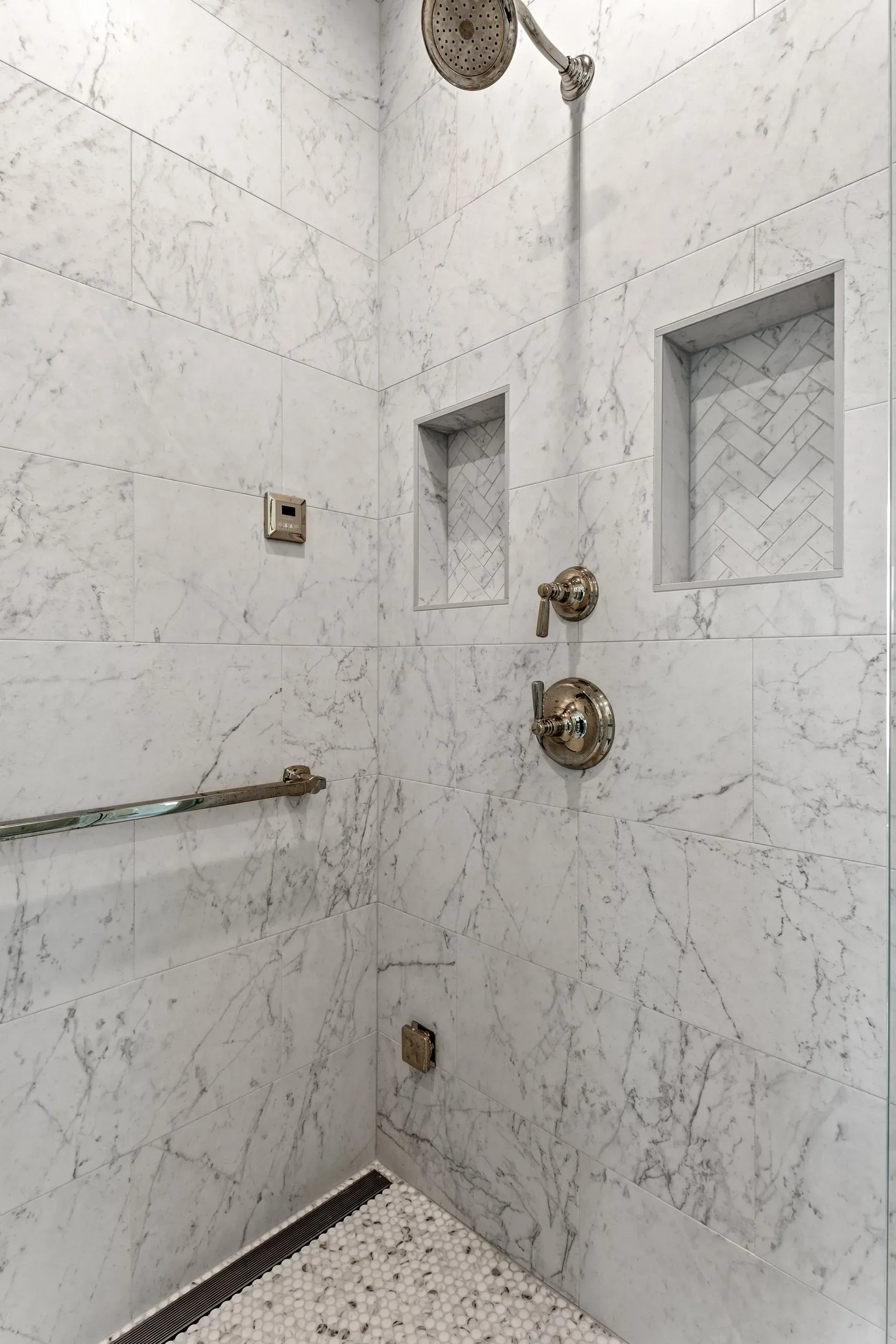 Marble-tiled shower with brass fixtures and built-in niches. Drain visible on the floor.