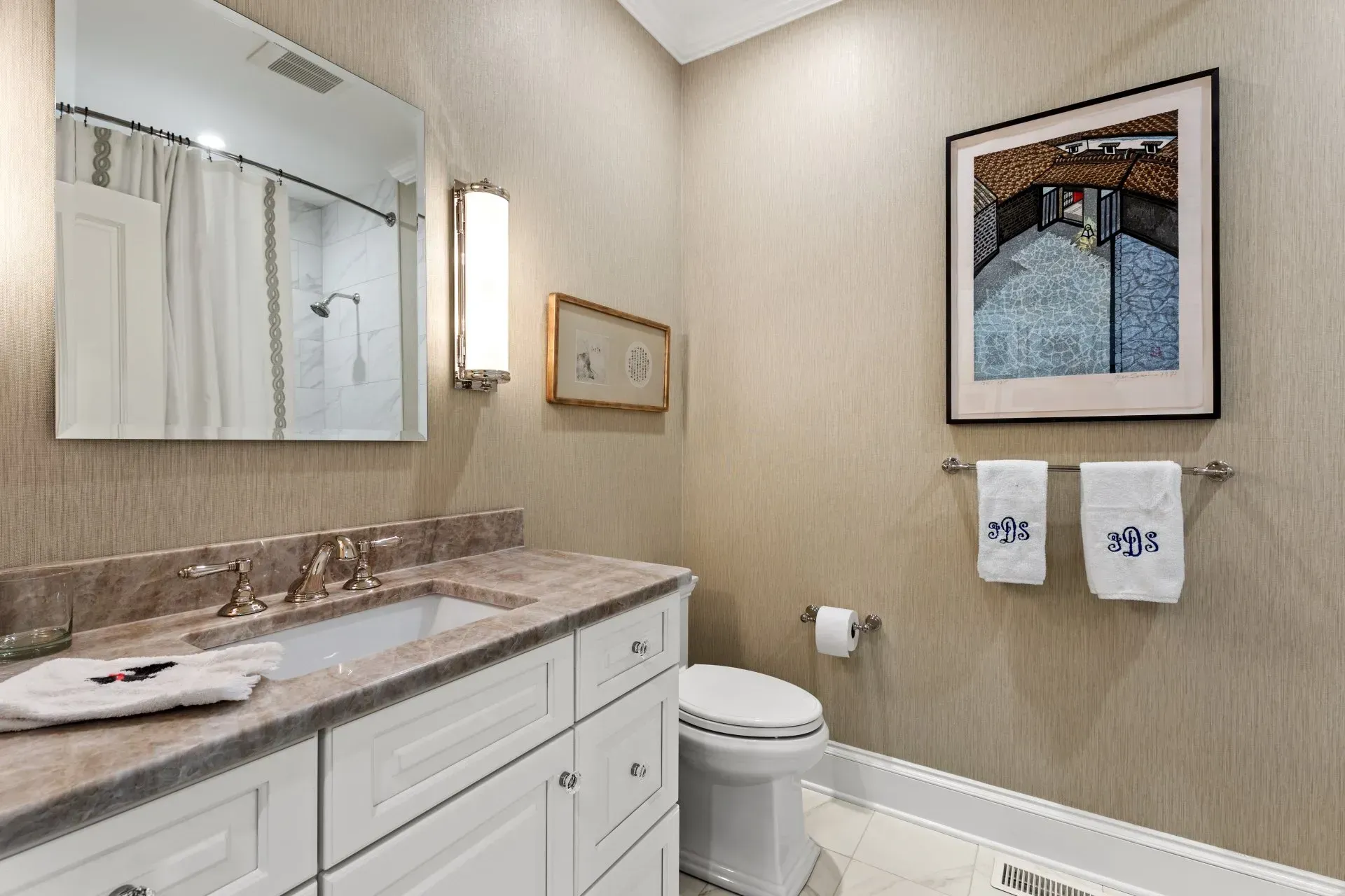 Bathroom with white cabinets, marble countertop, and neutral-toned walls. A framed picture hangs above the toilet.