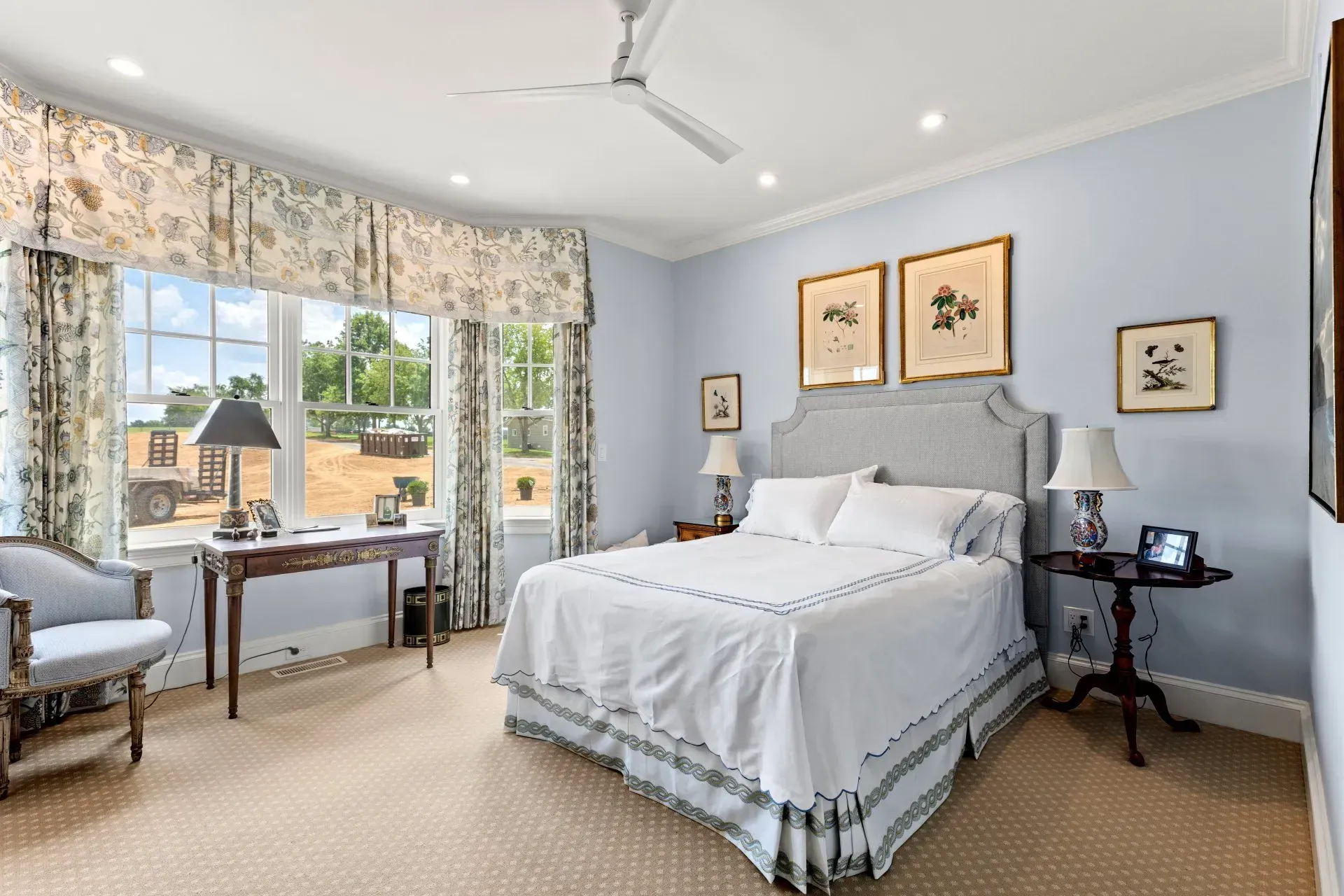 Bedroom with blue walls, white bedding, floral curtains, and framed botanical prints.