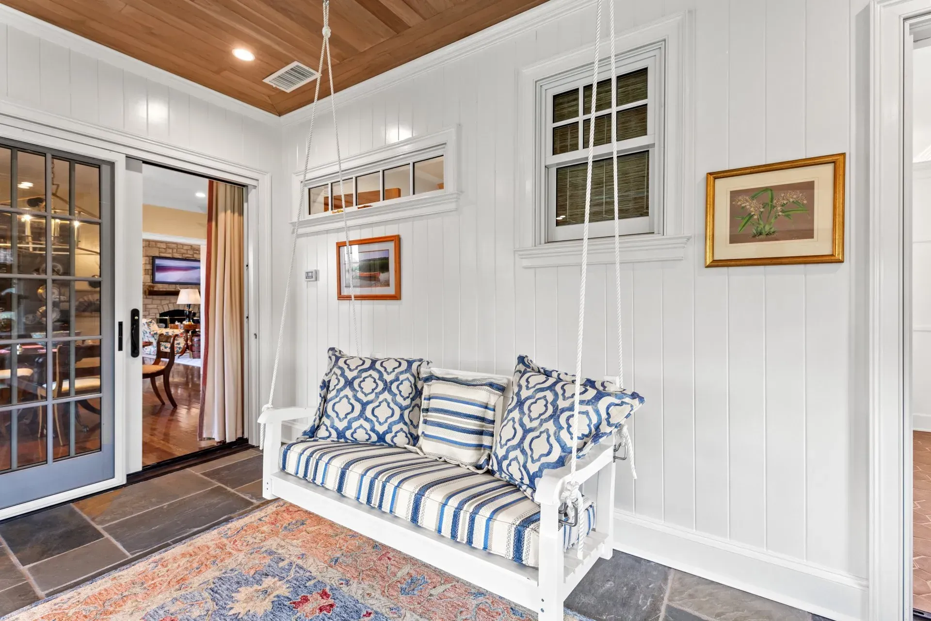 White porch with swing, blue patterned cushions, rug, and artwork.