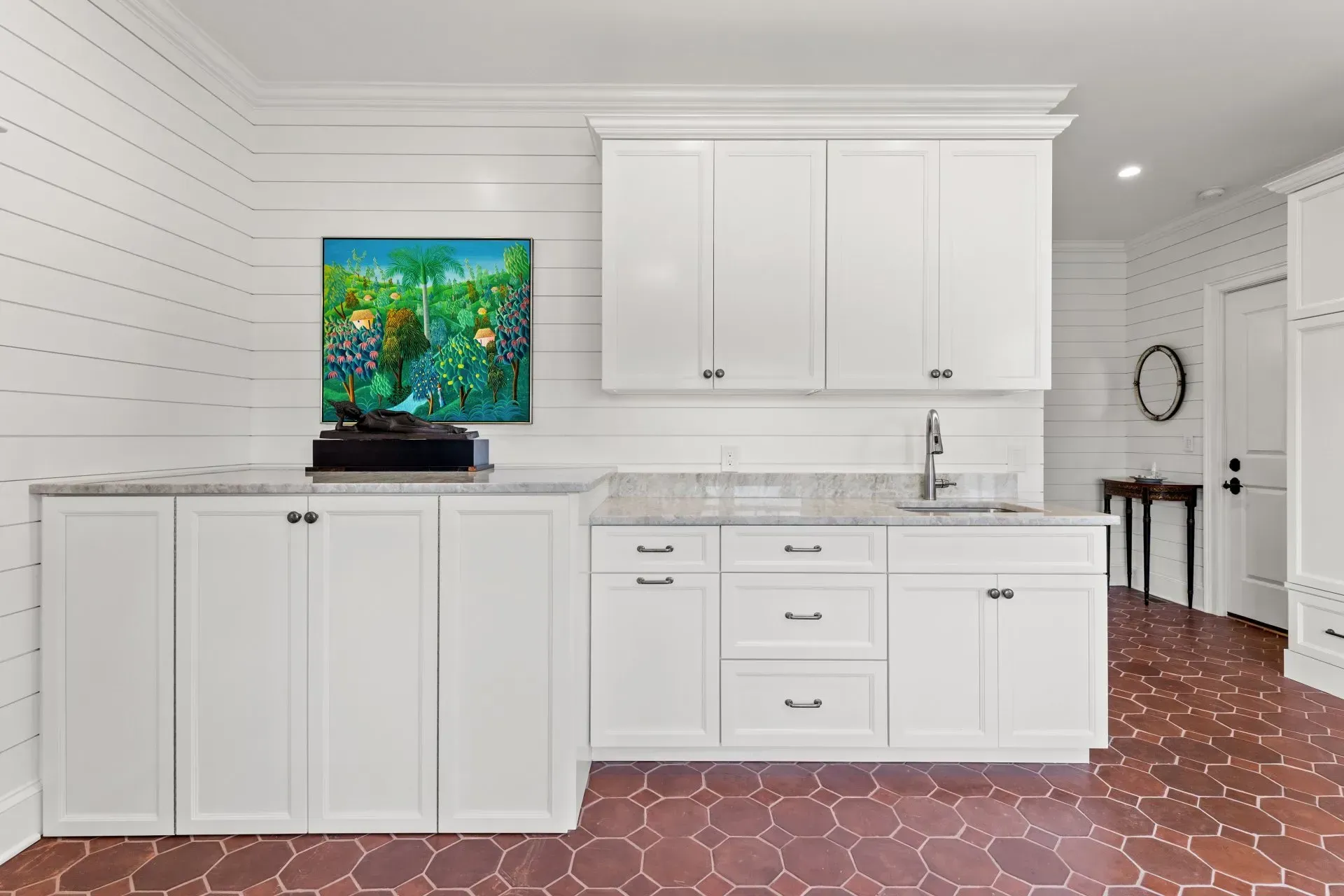 White laundry room with cabinets, sink, and artwork. Red tile floor.