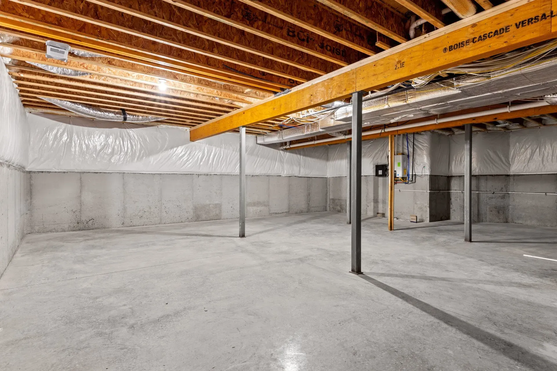 Empty unfinished basement with concrete walls and floor, wooden beams, and support columns.