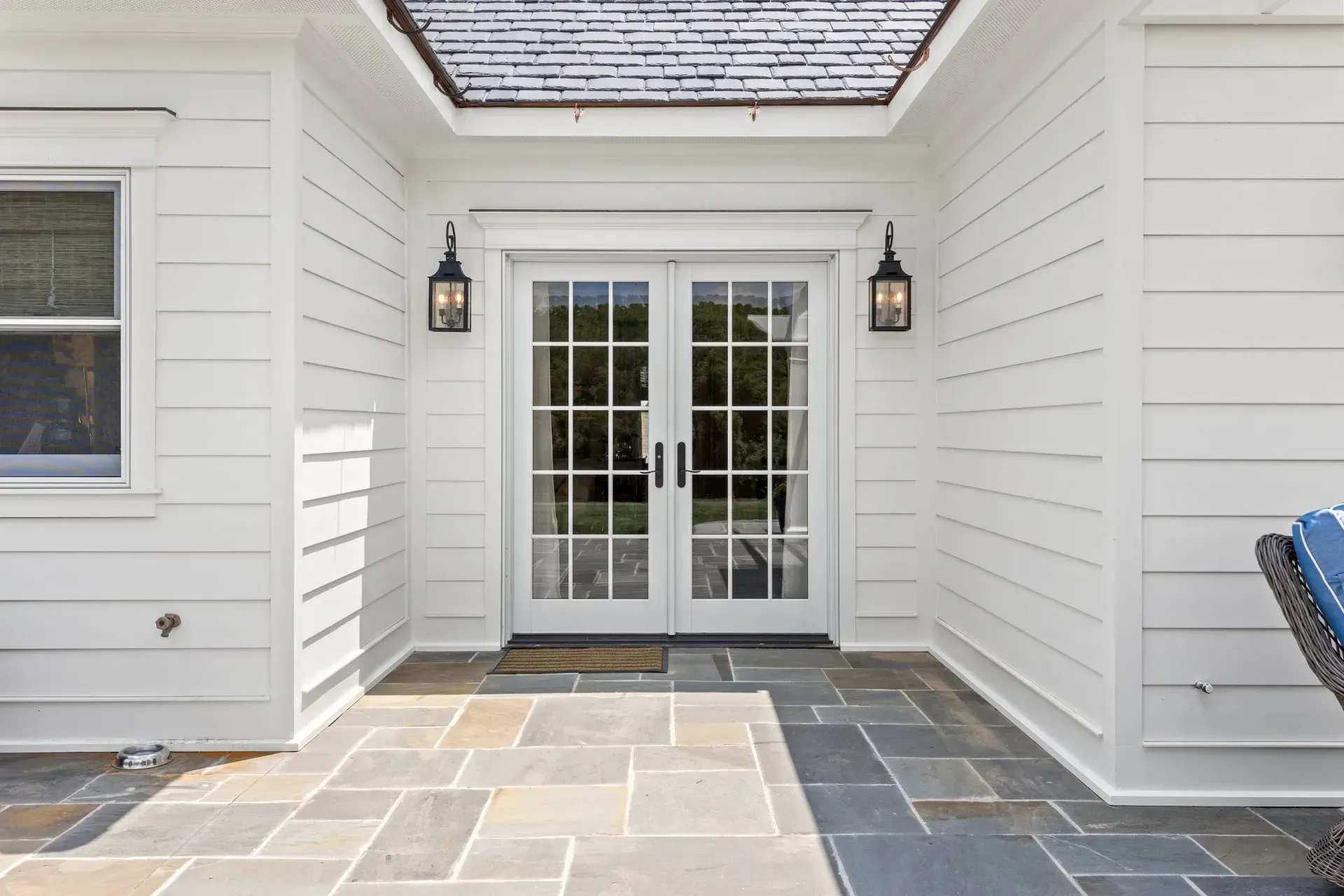 White double doors with glass panes, flanked by wall sconces, on a stone patio.