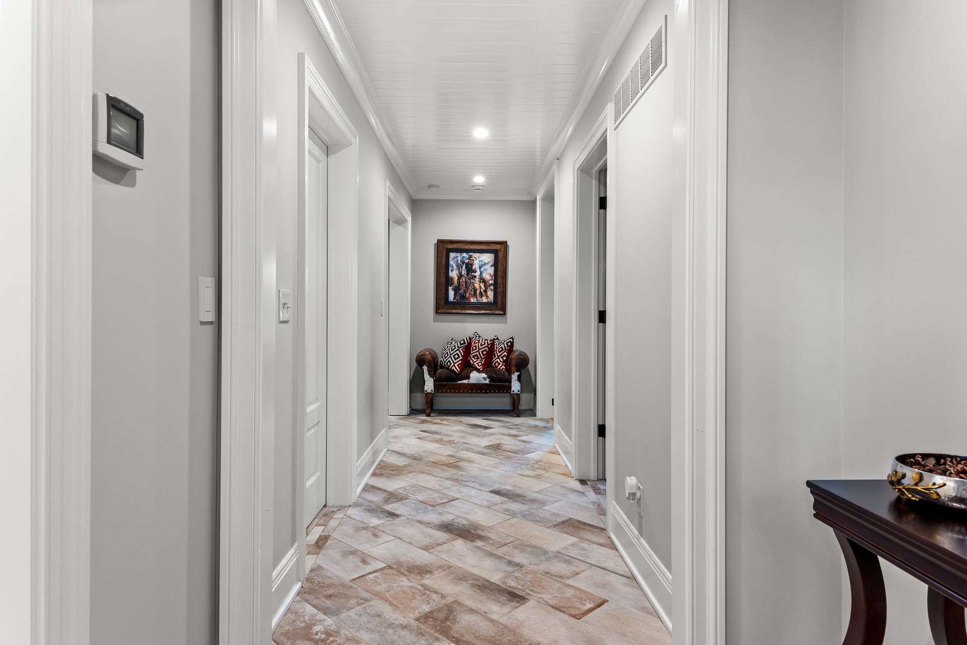 Hallway with patterned tile floor, white trim, gray walls, and a small table at the end.