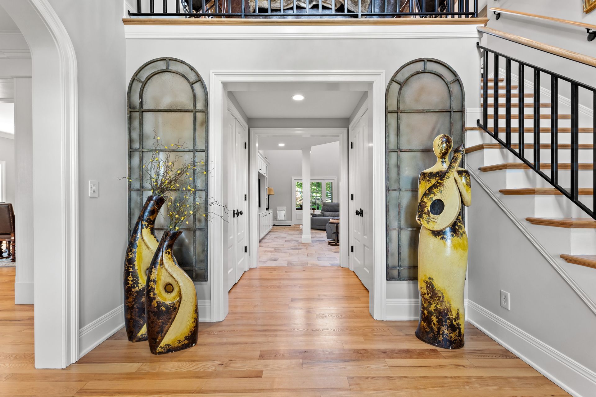 Entryway with hardwood floor, tall arched windows, decorative vases, and a staircase.