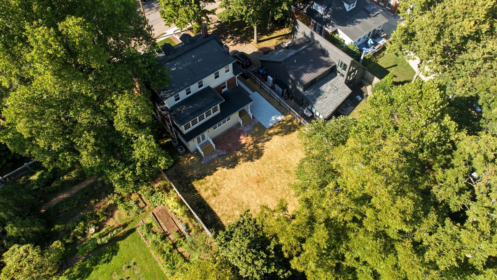 Aerial view of a house with a brown roof and yard surrounded by green trees and a fence.