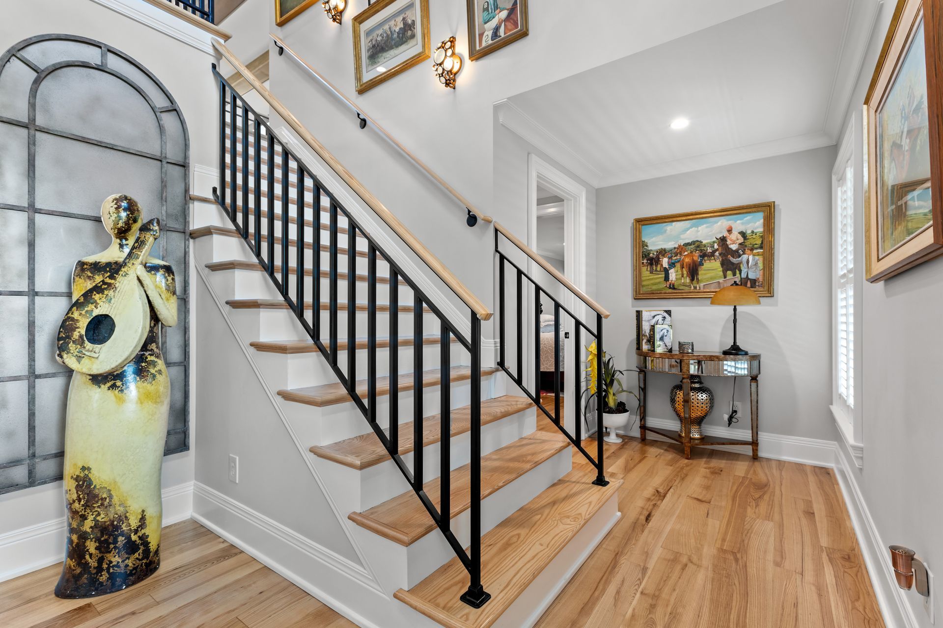 Staircase with black railing, wooden steps, and a decorative statue by a large window.