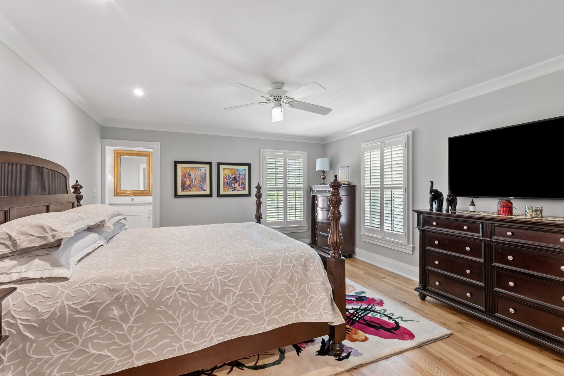 Bedroom with bed, dresser, TV, artwork, and window with shutters.
