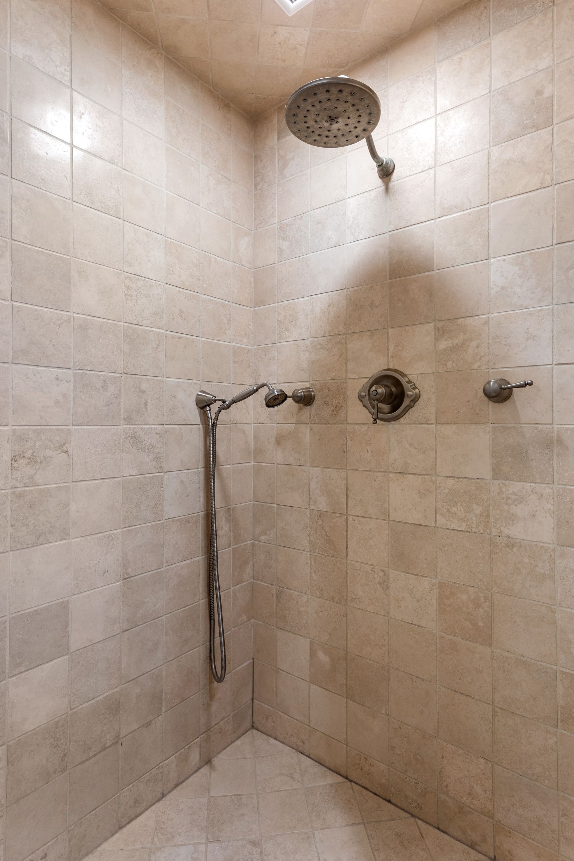 Shower with beige tile walls and silver fixtures.