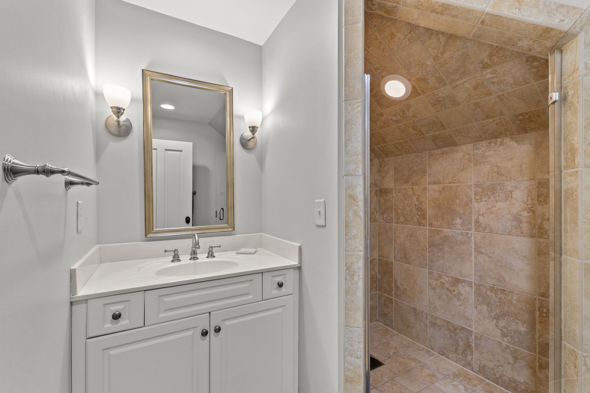 Small bathroom with vanity, mirror, sconces, and a tiled shower stall.