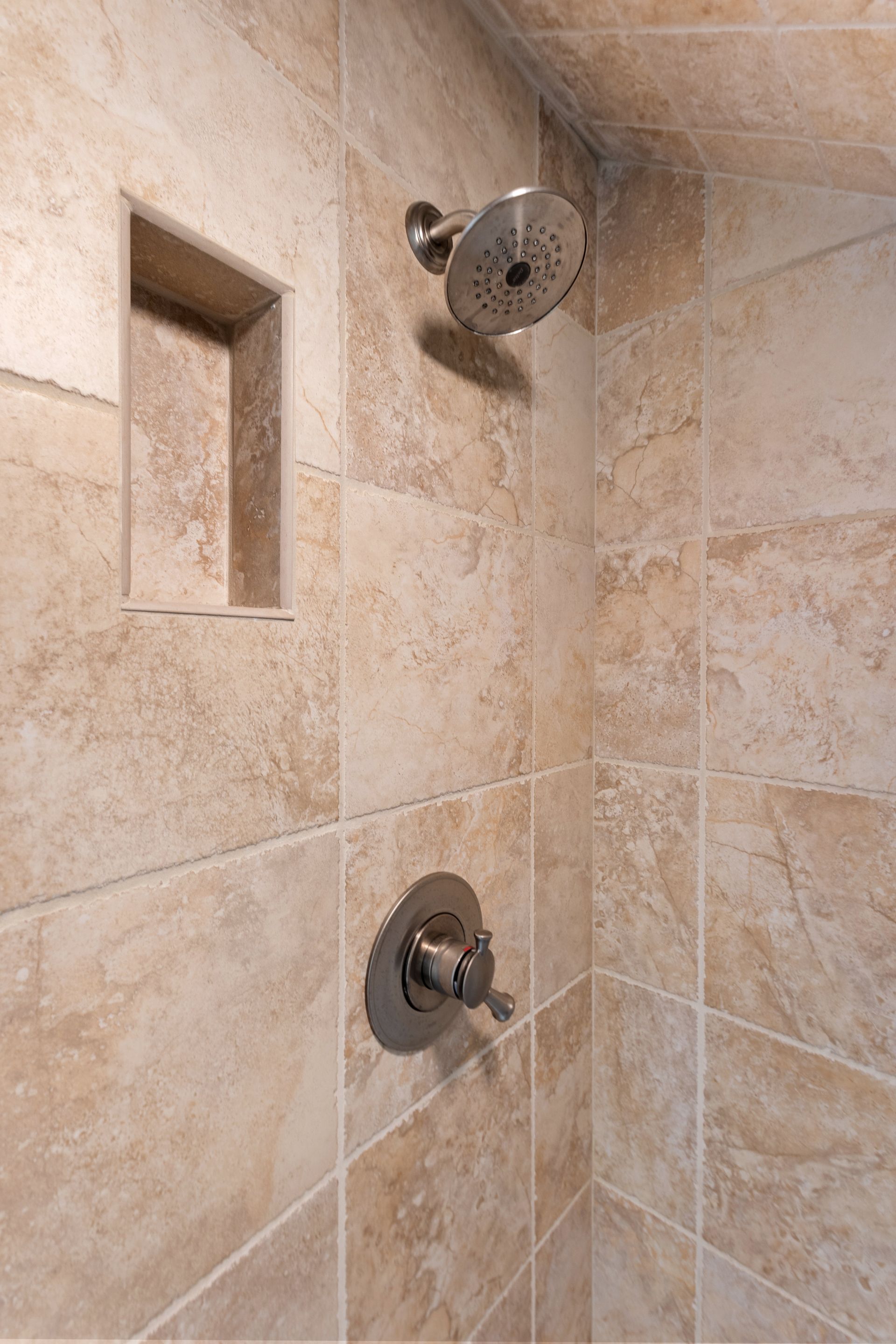 Shower with beige tiles, stainless steel showerhead, and a niche for storage.