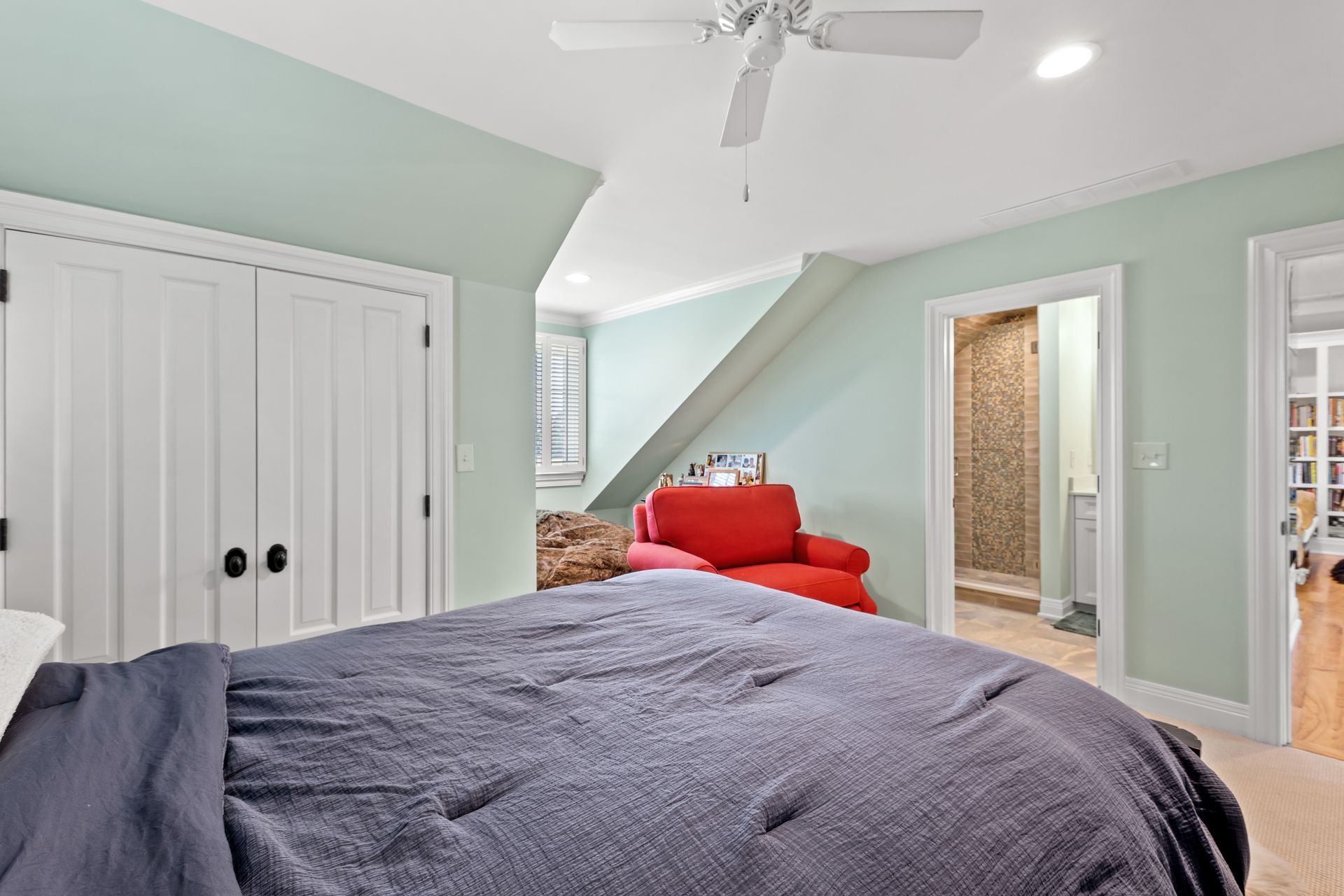 Bedroom with blue bed, red chair, white closet, green walls, and doorway to shower.