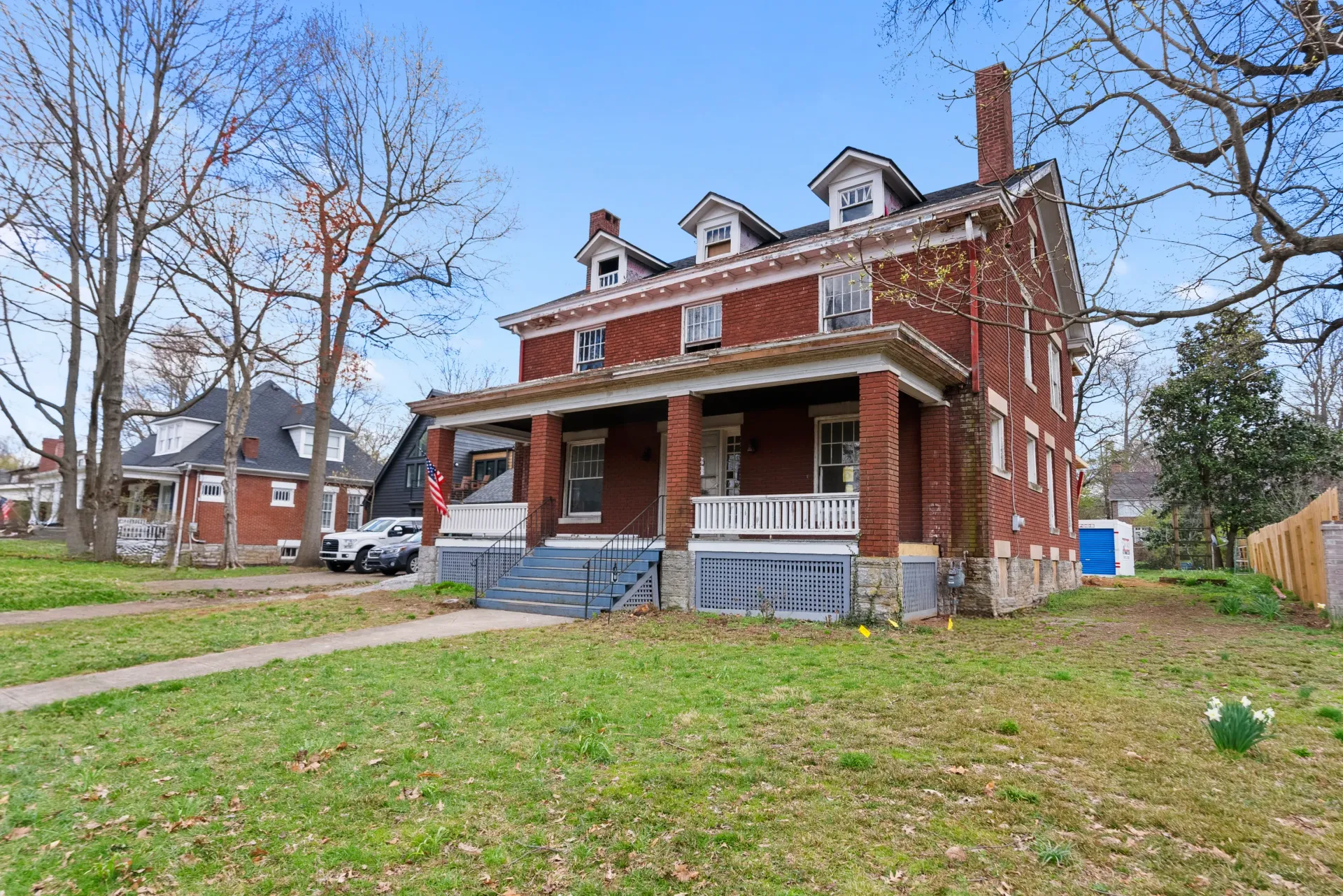 A brick three-story house with a front porch, blue sky, and leafless trees.