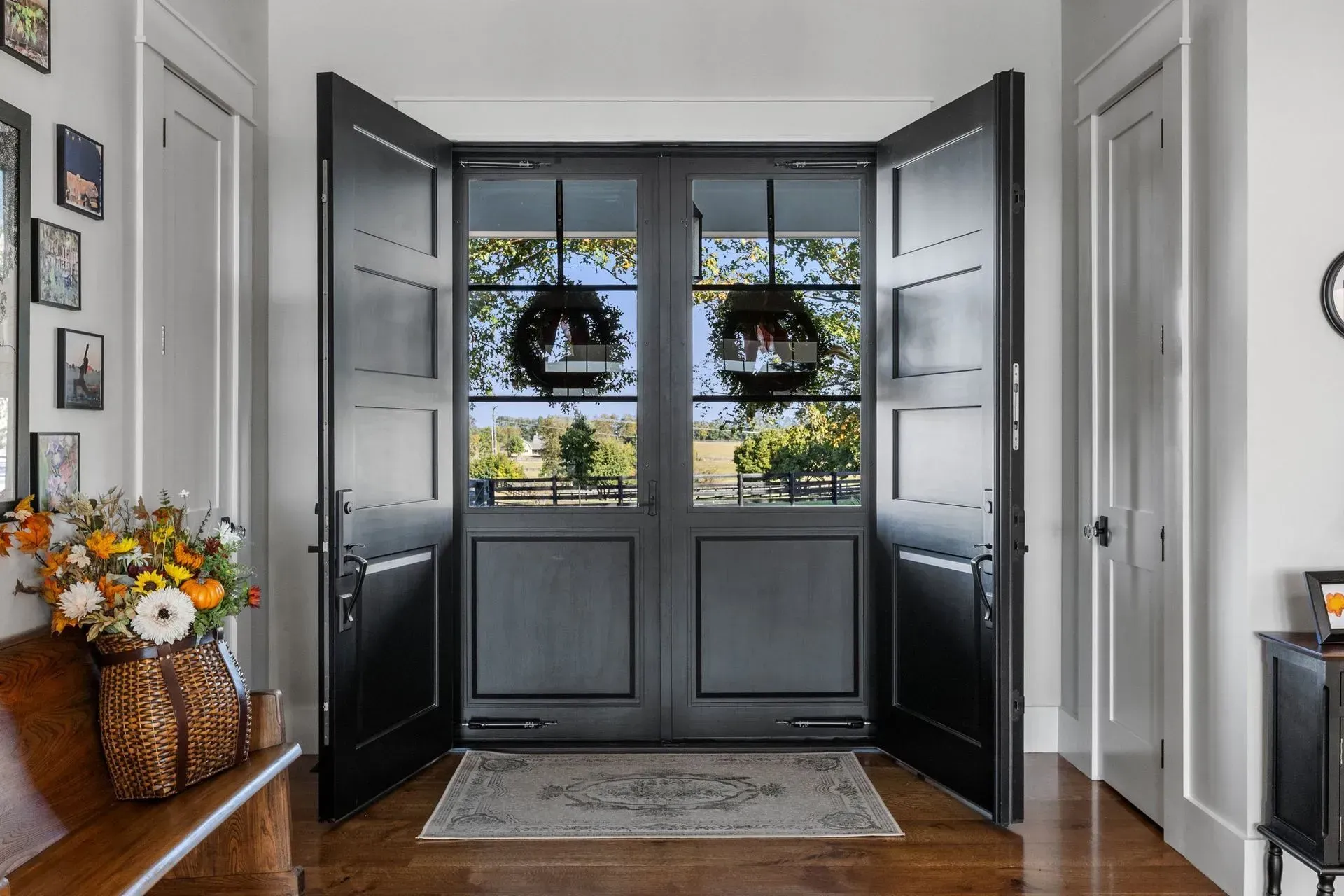 Black double doors open to a sunny outdoor view, flanked by white trim and a flower arrangement.