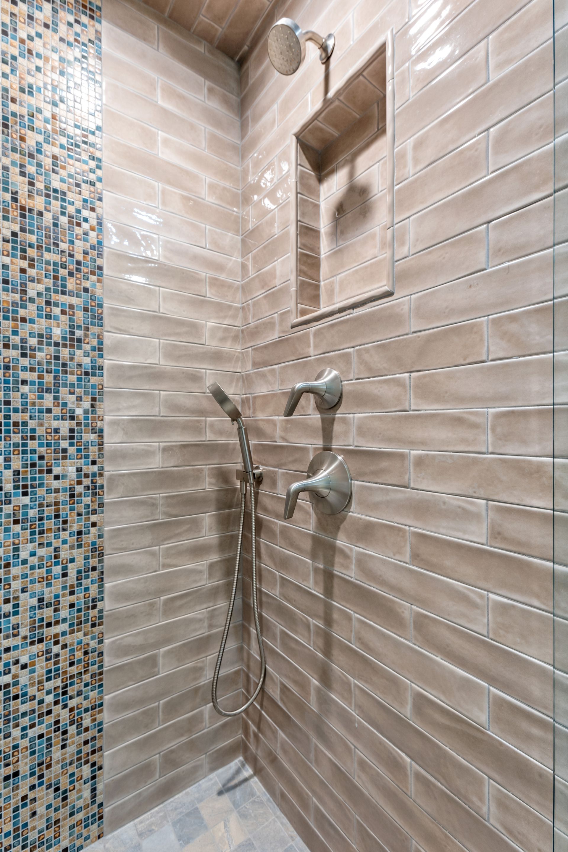 Shower with beige brick tiles and a blue mosaic accent. Handheld shower and built-in shelf.