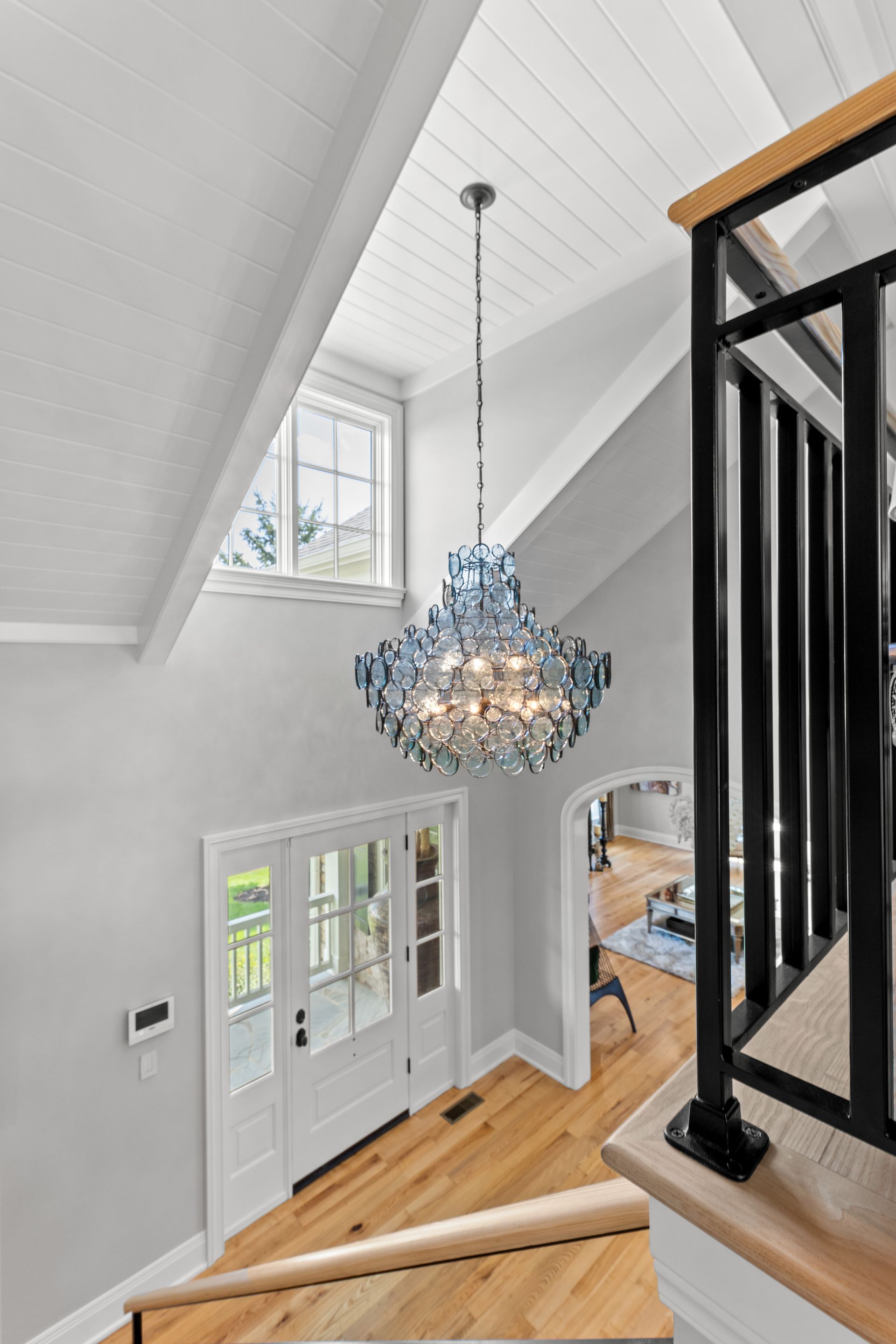 A bright entry with a chandelier above a wooden staircase, white door, and black railings.