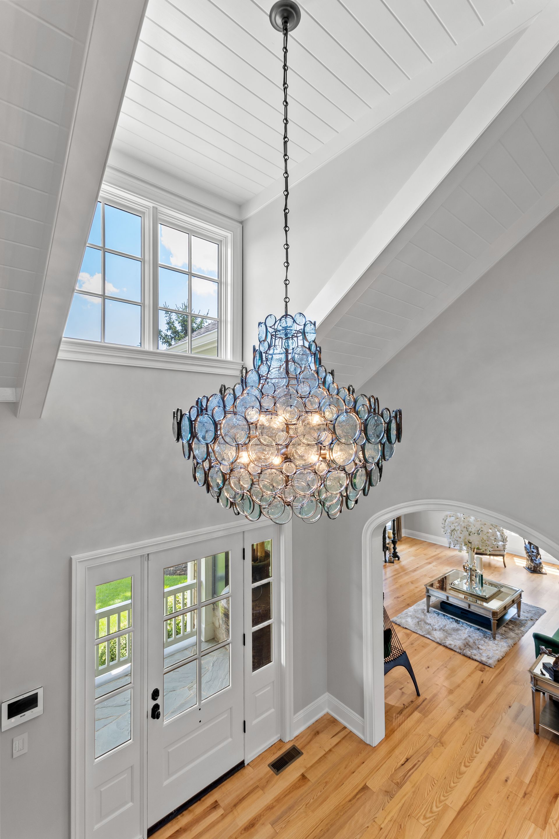 Chandelier in a light-filled entryway with high ceilings, window, and a glimpse of the living room.