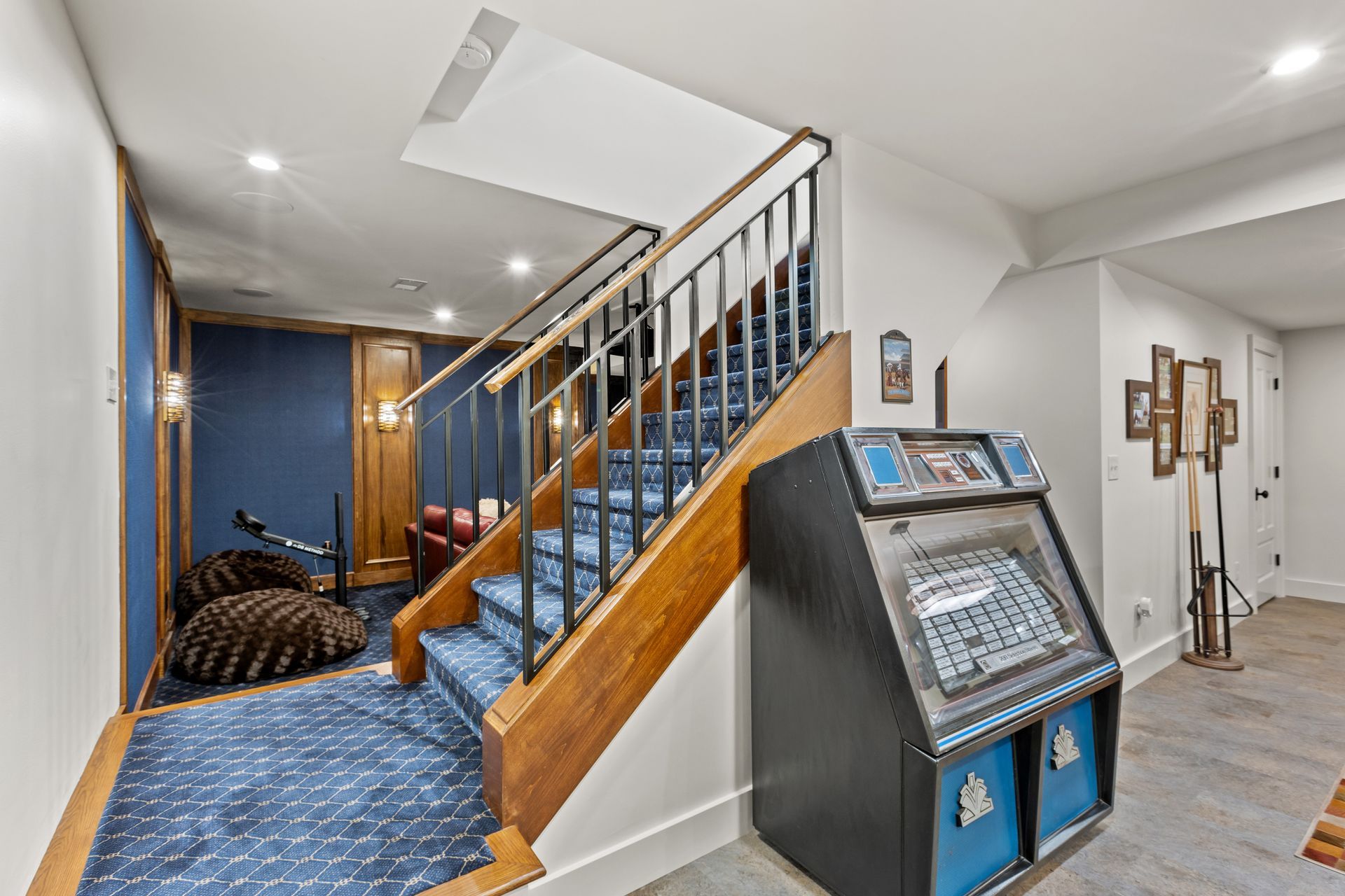 Arcade game next to stairs leading down to a game room with blue carpet and walls.