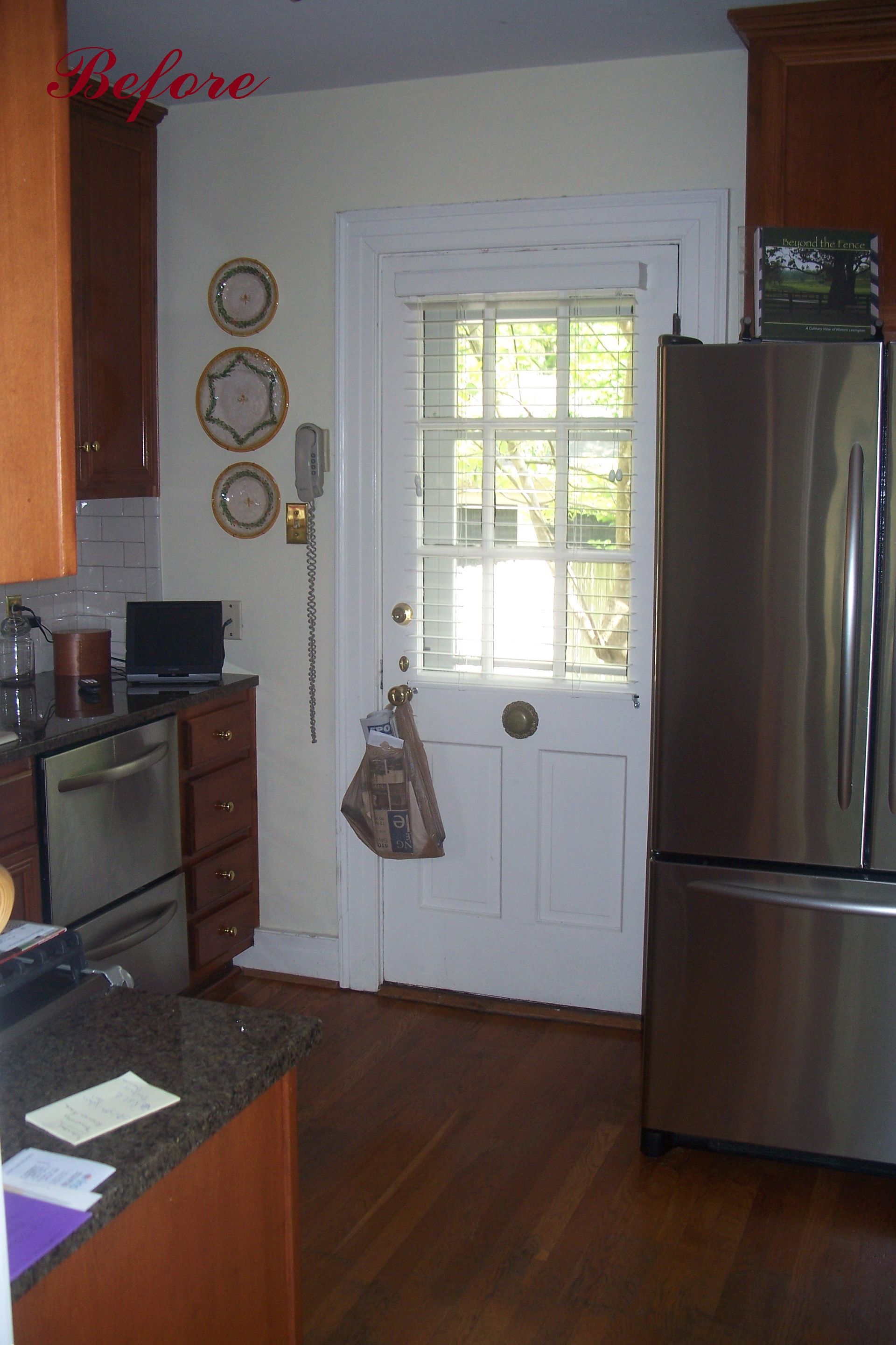 Kitchen before renovation: brown cabinets, stainless steel appliances, white door, wood floor.