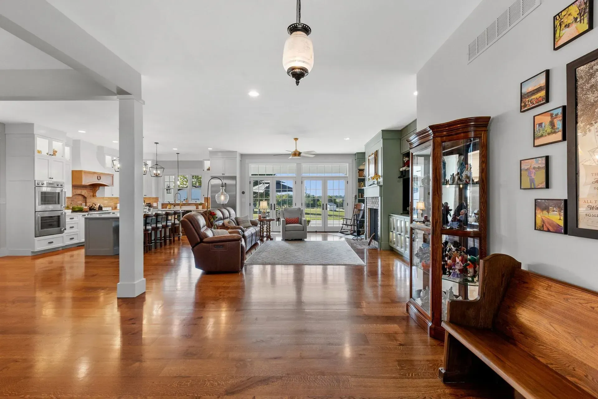 Spacious home interior: hardwood floors, open layout, kitchen, living room with view, artwork and antique bench.