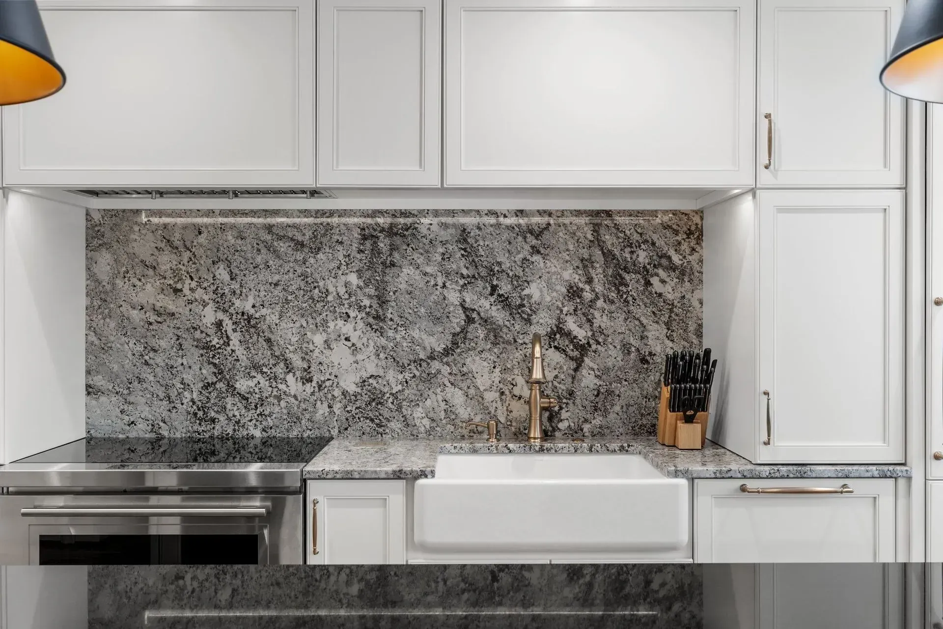 White kitchen with granite backsplash, stainless steel appliances, and farmhouse sink.