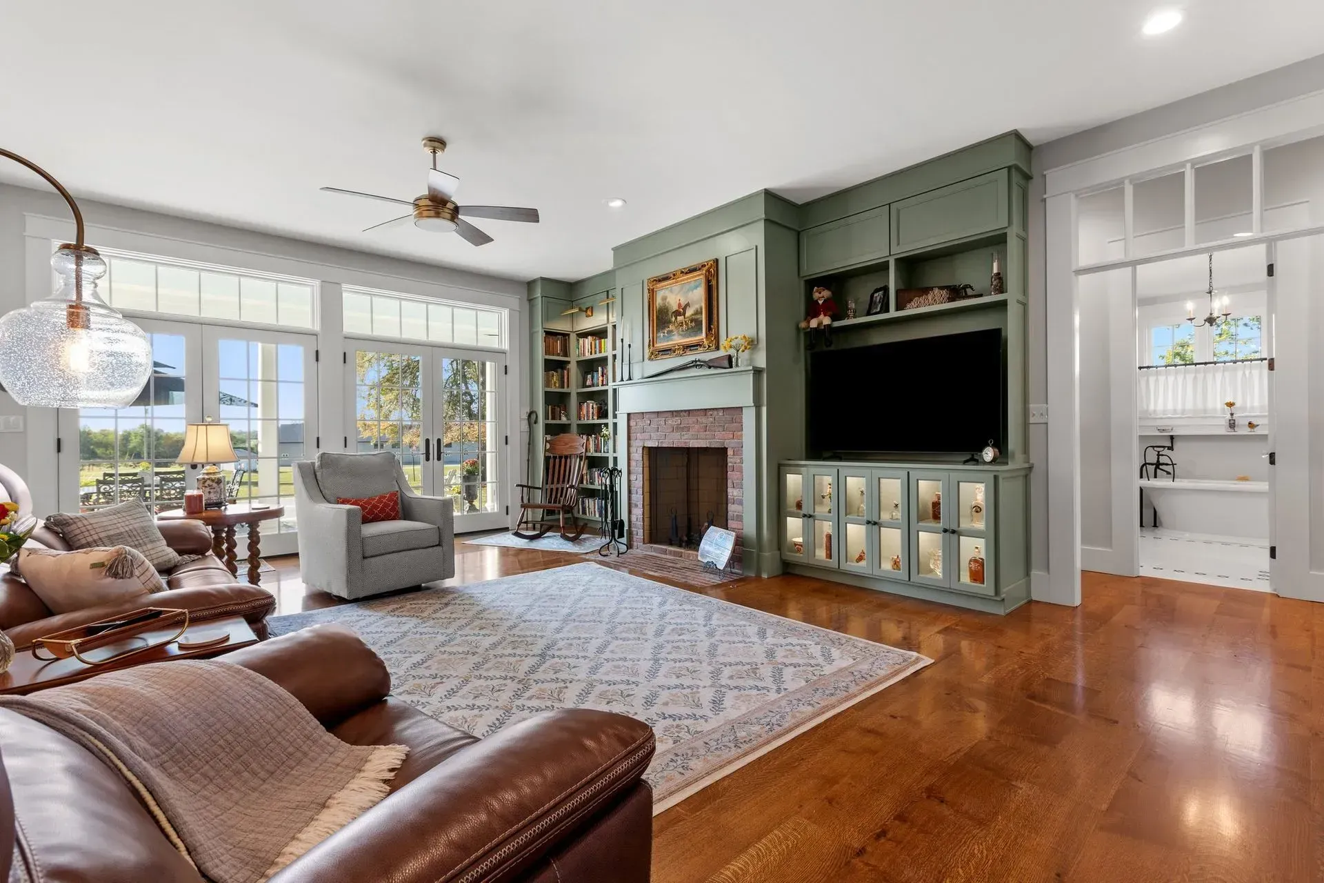 Spacious living room with fireplace, built-ins, and brown leather furniture, next to glass doors.