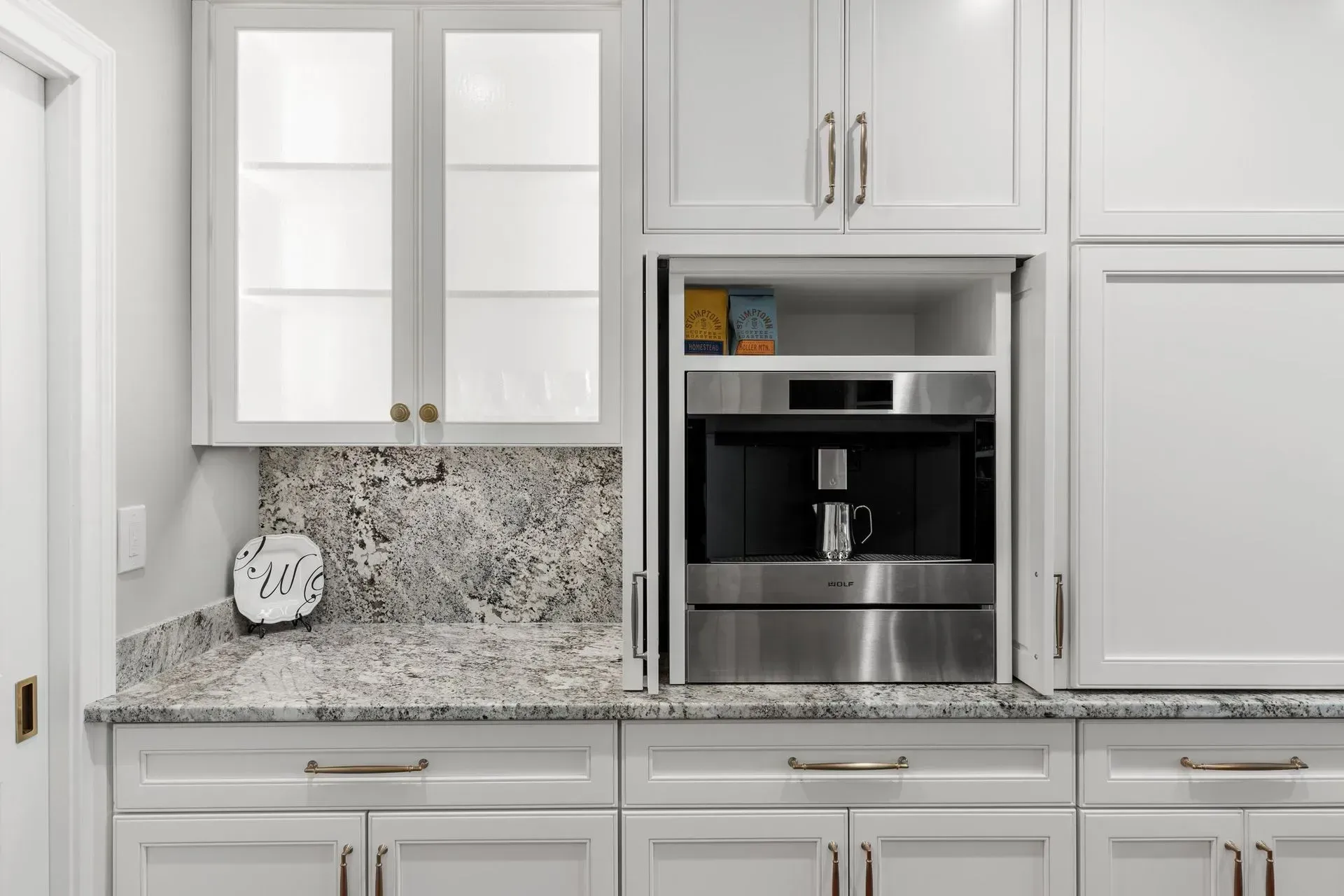 White kitchen cabinets with built-in coffee maker; granite countertop, light and bright.