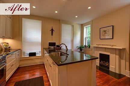 Remodeled kitchen with island, fireplace, and windows; cream cabinets, dark countertops, and wood floors.