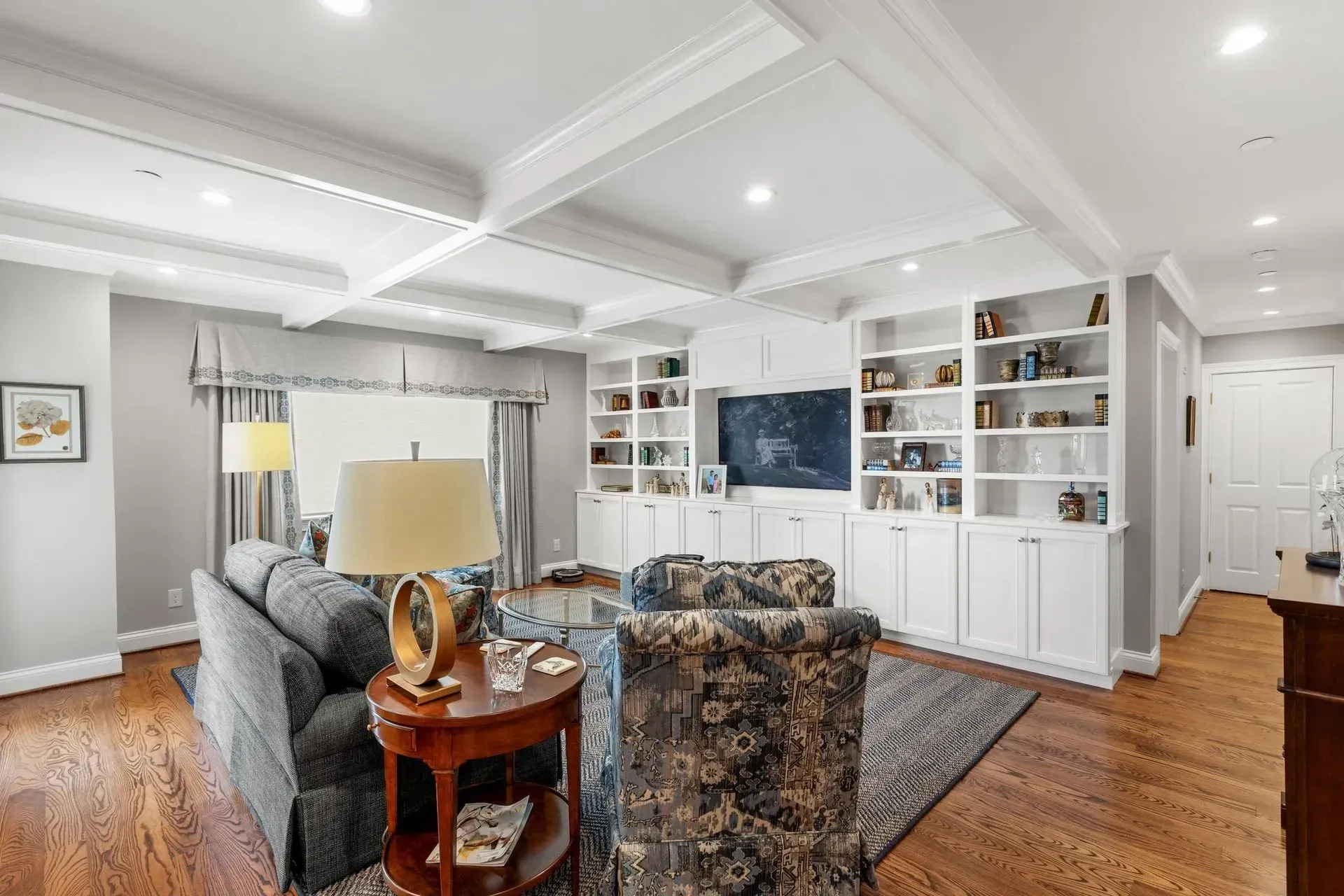 Living room with built-in white bookshelves, hardwood floors, gray walls, and blue patterned furniture.