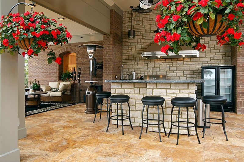 Outdoor bar with stone facade, stools, cooler, and hanging red flowers.